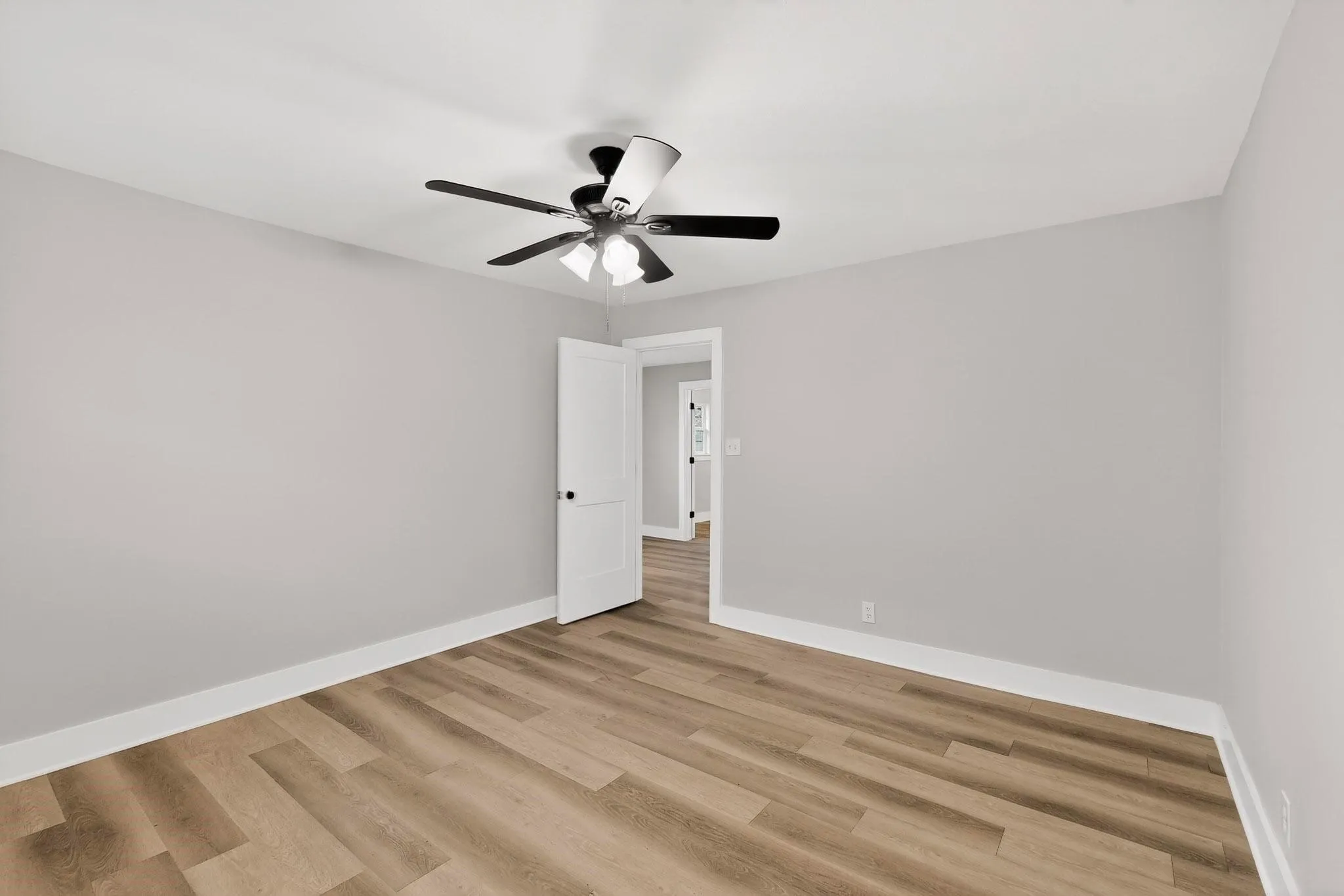 Room featuring wood-finish flooring, light gray walls, white baseboards, and a ceiling fan with integrated lighting