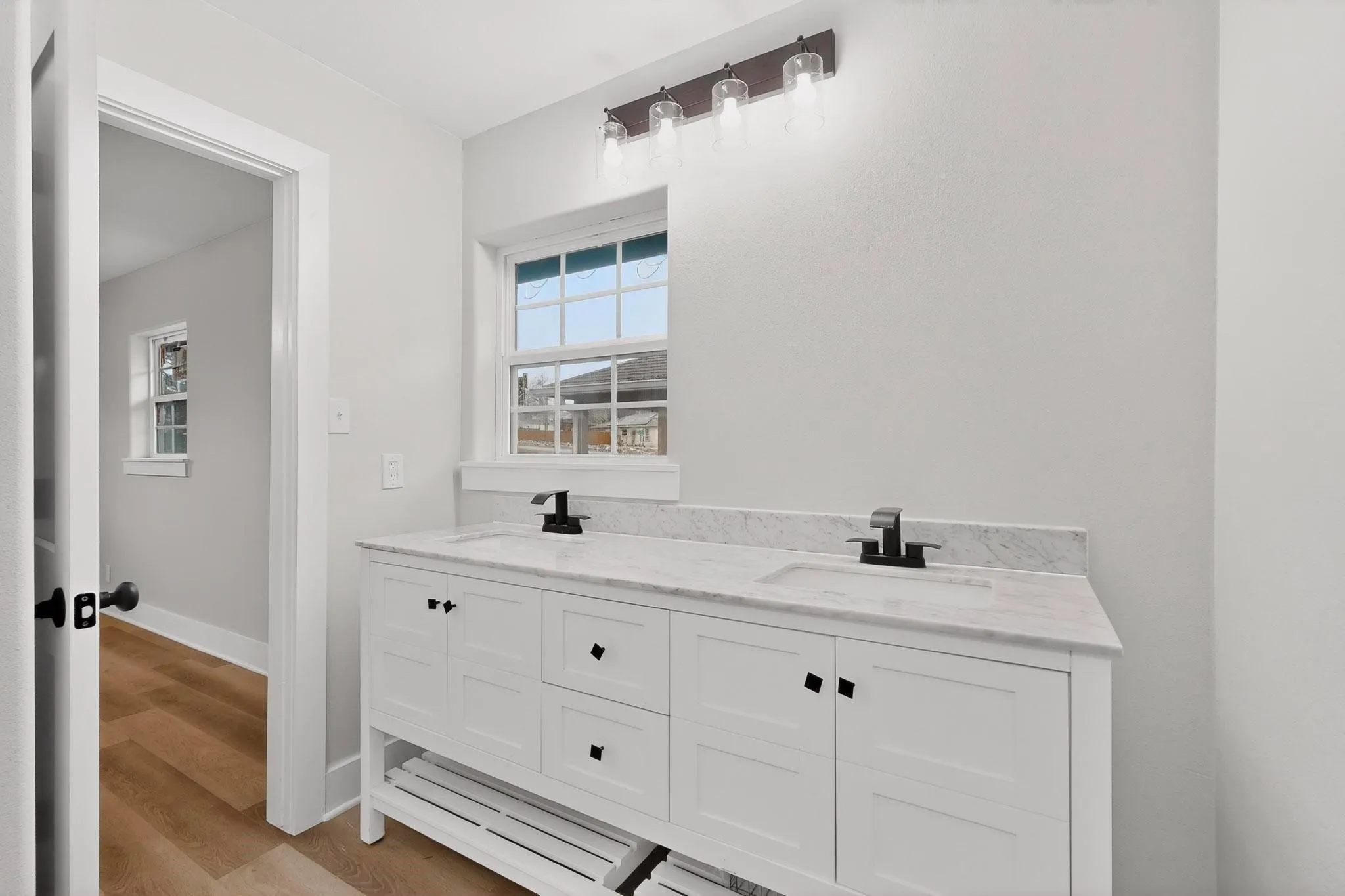 White dual vanity with integrated sinks, a stone countertop, black hardware, and an overhead four-bulb light fixture