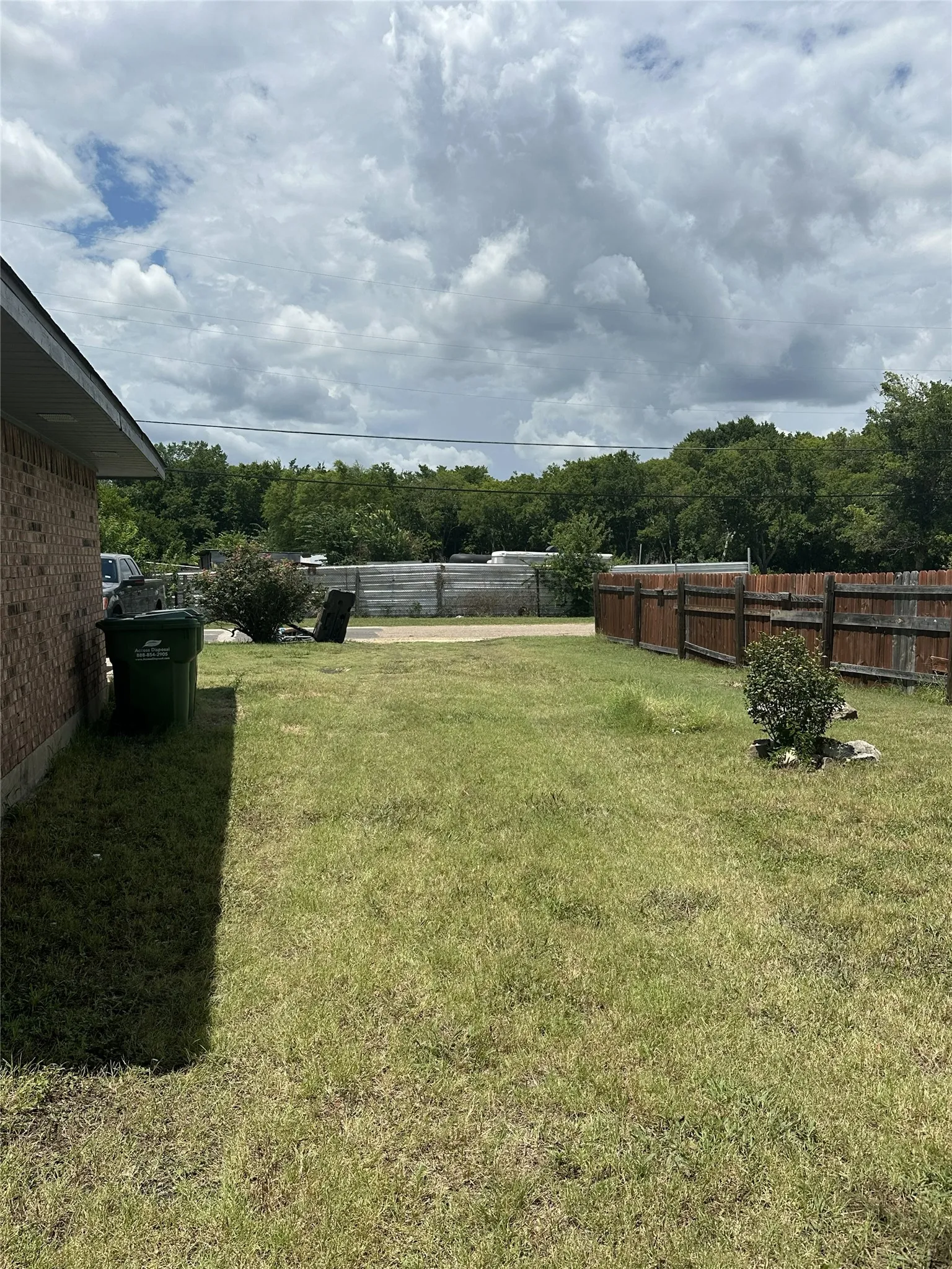 Expansive grassy yard featuring a wood privacy fence, brick exterior siding, and mature perimeter trees
