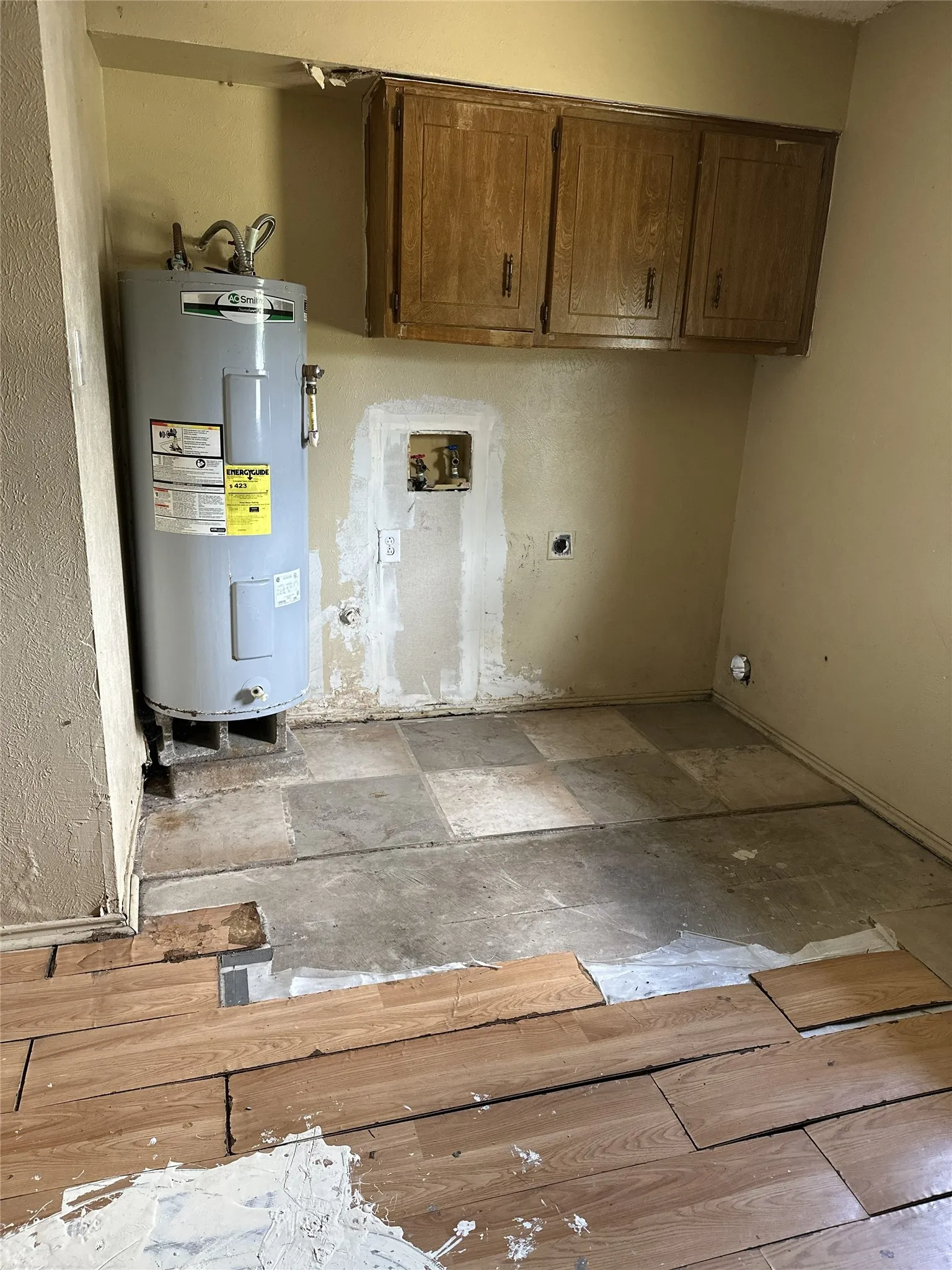 Garage conversion - Utility space featuring a water heater, upper cabinetry, and mixed flooring with wood-finish planks and tile