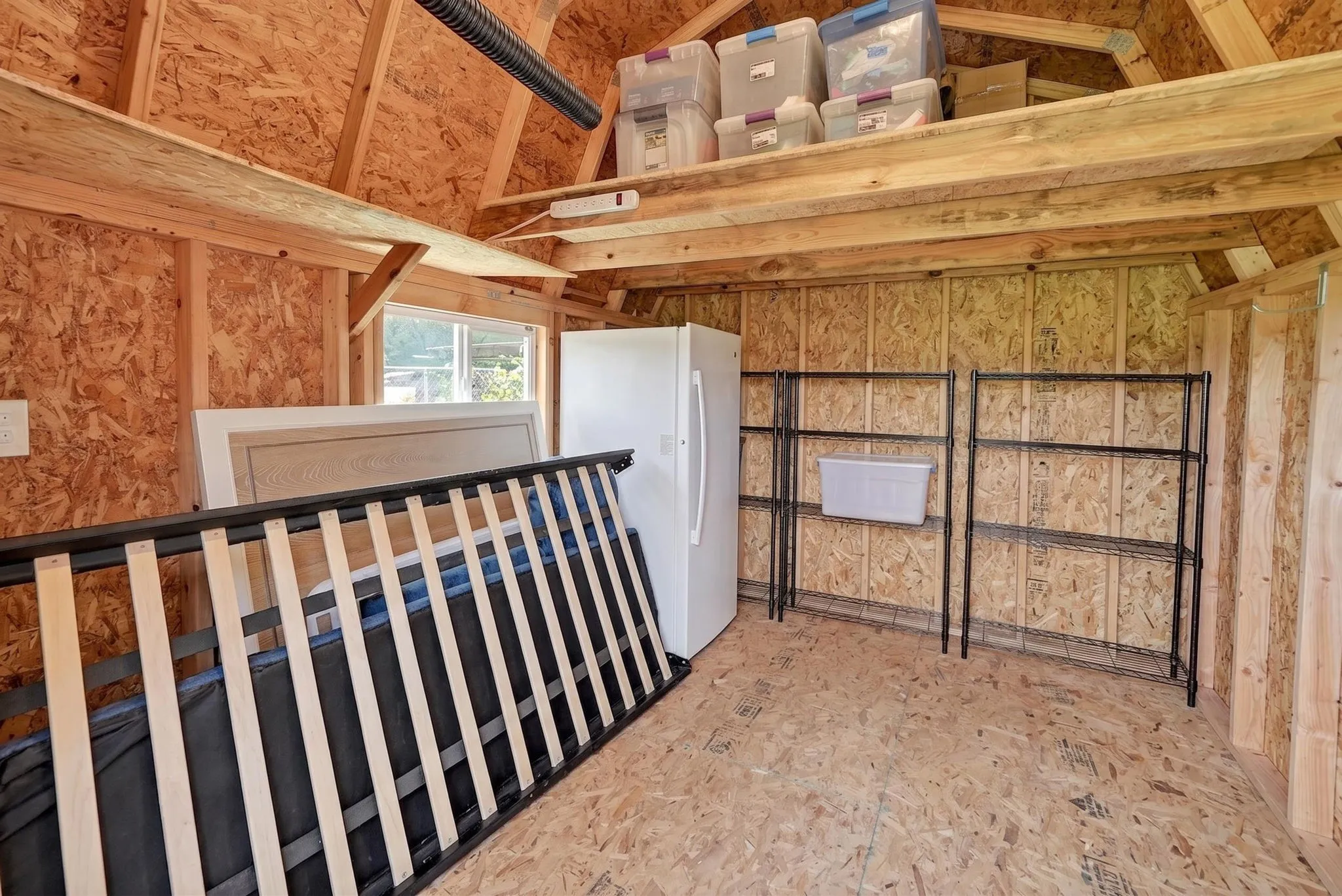 Storage shed interior featuring exposed oriented strand board walls and flooring, a vaulted ceiling, a small window, and an overhead storage loft