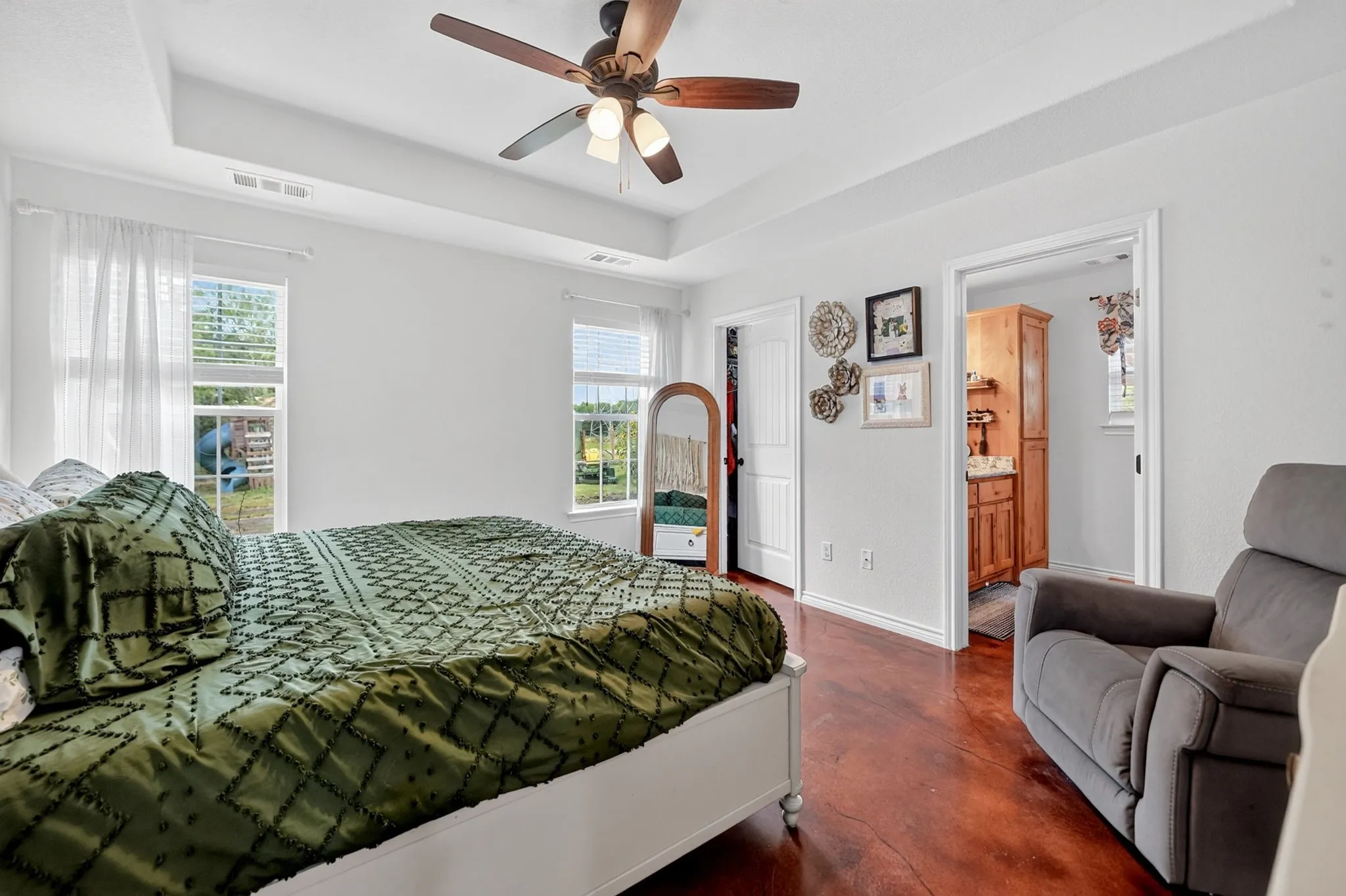 Spacious room featuring rich wood-finish flooring, a tray ceiling, and a ceiling fan with integrated lighting