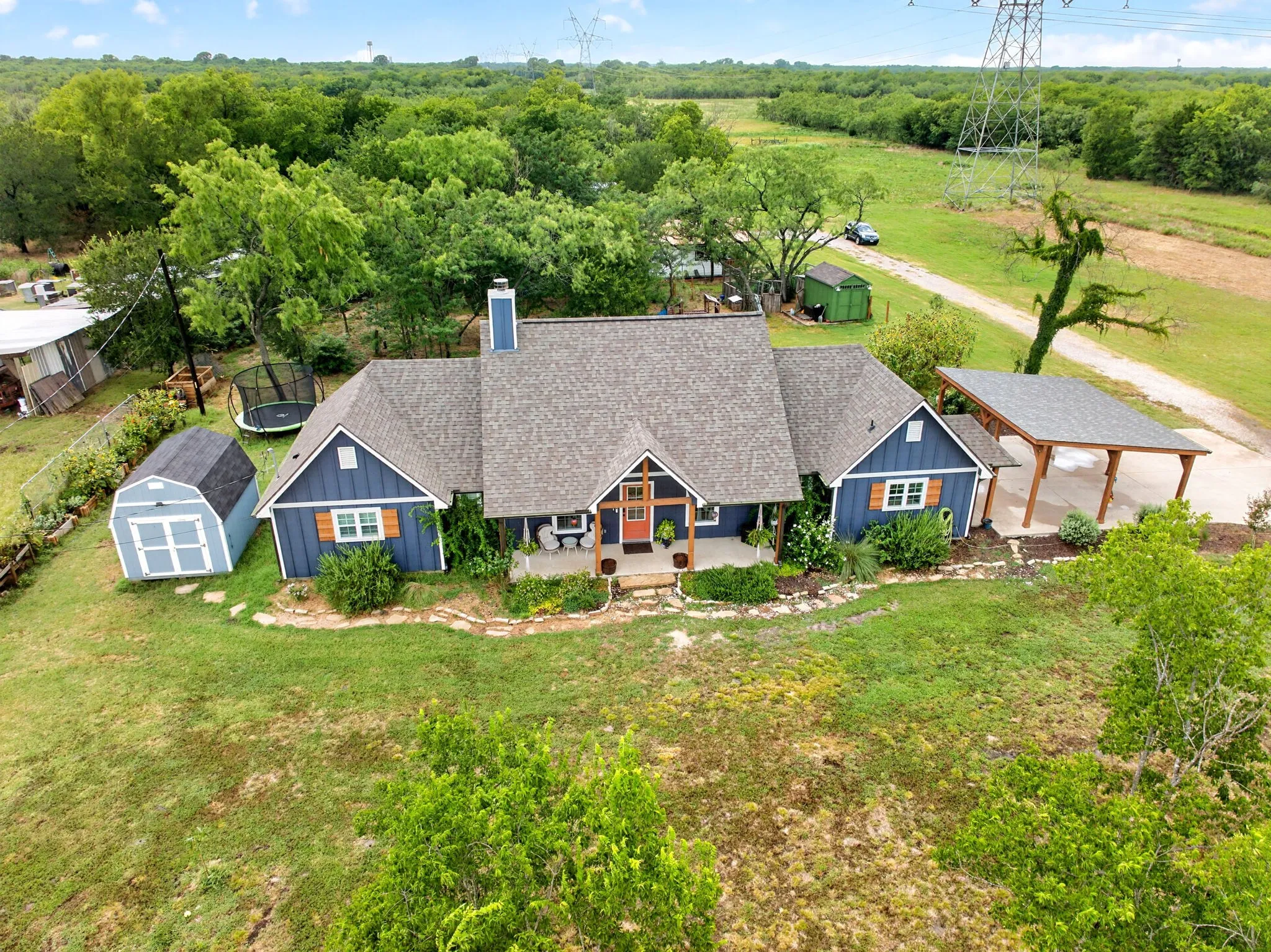 Blue siding residence featuring a covered front porch, a shingle roof, and a detached carport with a shingle roof