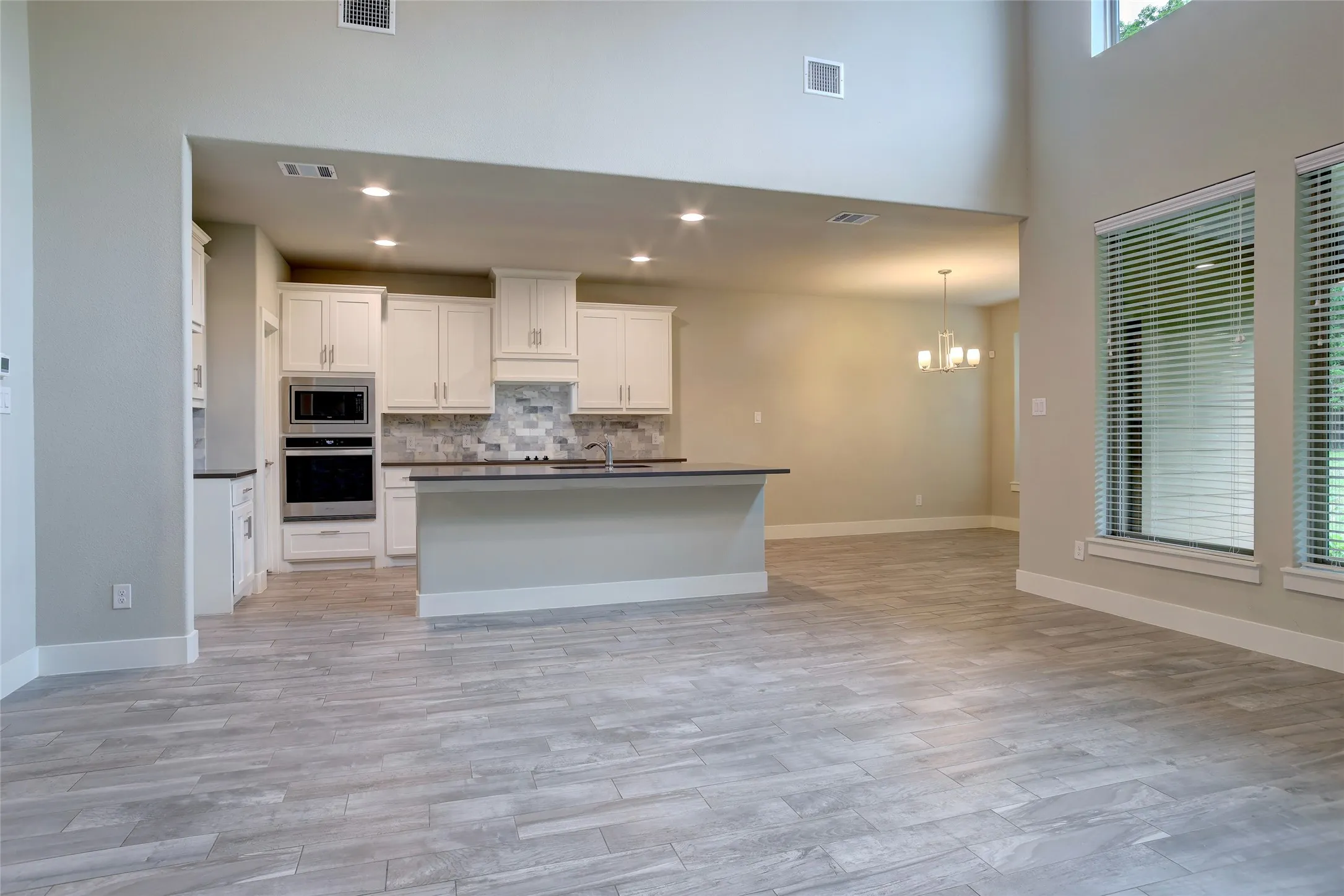 Open-concept kitchen featuring white cabinetry, built-in stainless steel appliances, a tiled backsplash