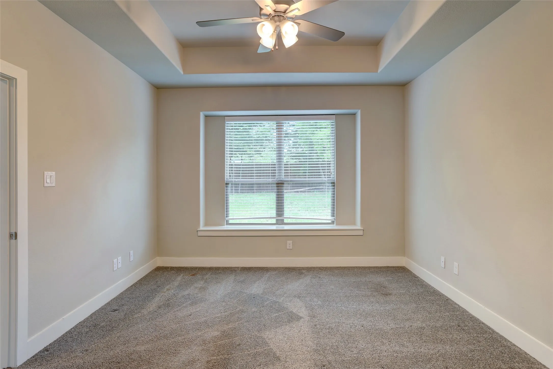 Bedroom featuring a tray ceiling, recessed window with blinds, and a ceiling fan with integrated lighting