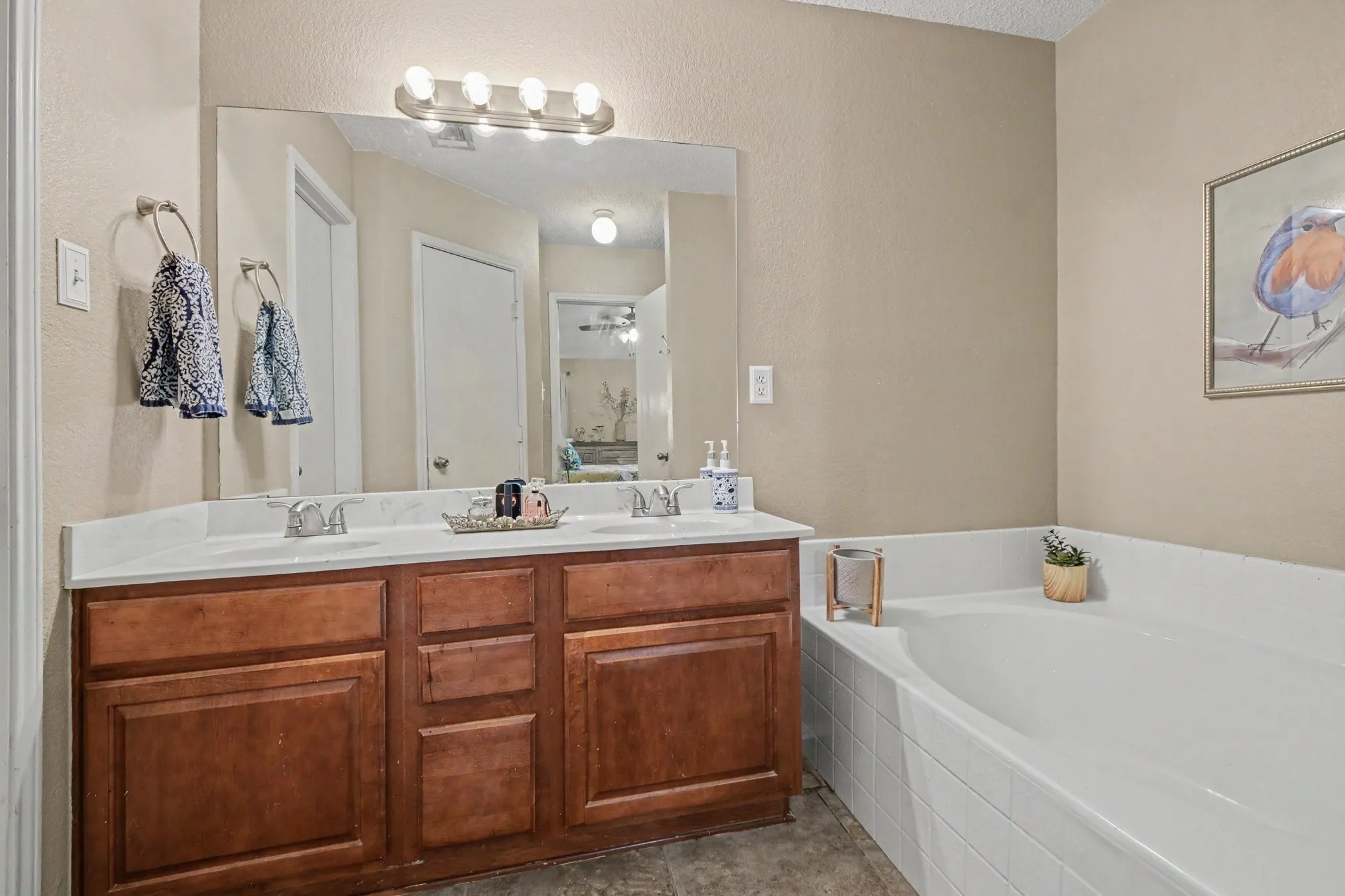 Bathroom featuring a double vanity with wood-finish cabinetry and white countertops, a large mirror, and a built-in bathtub with white tile surround