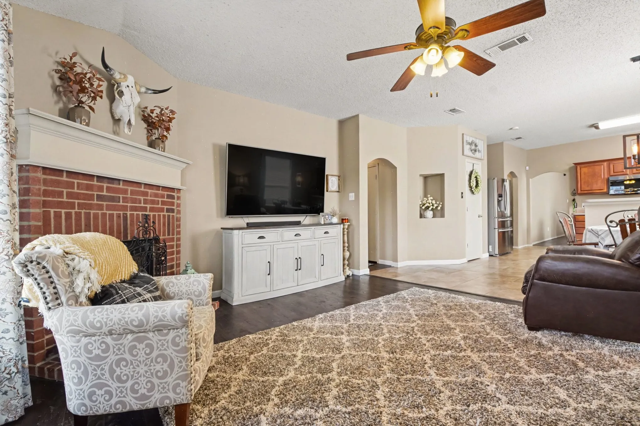 Living area featuring a brick fireplace with mantel, dark wood-finish flooring, and a ceiling fan with integrated lighting