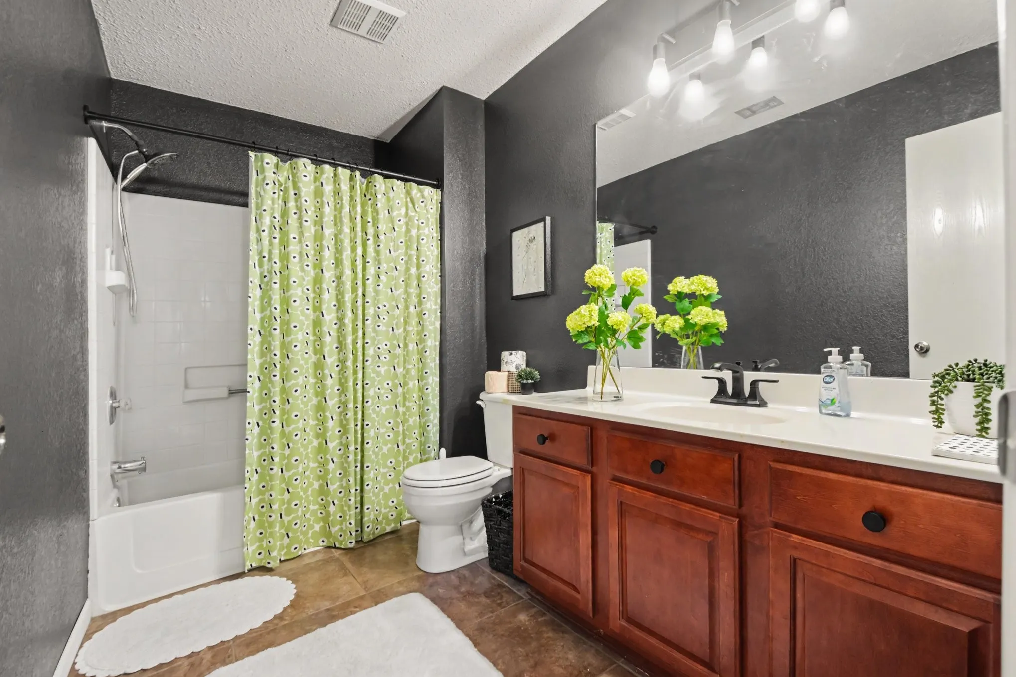 Bathroom featuring a white tub and shower combination, a dark wood-finish vanity with a white countertop, a black-finish faucet, and a large wall-mounted mirror
