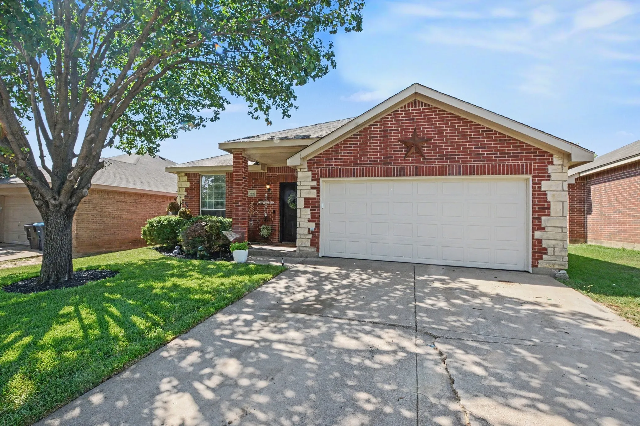Brick and stone facade residence featuring an attached two-car garage, a concrete driveway, and a mature tree