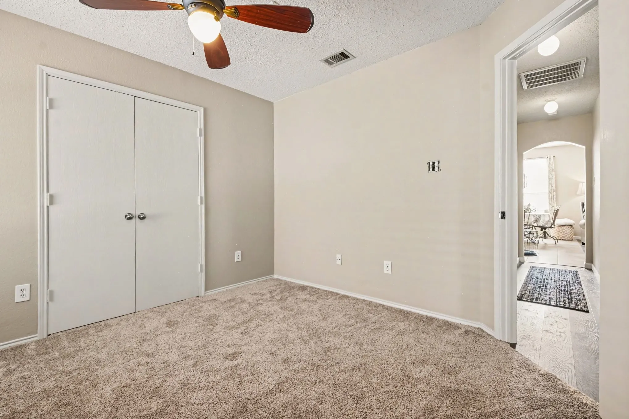 Spacious room featuring neutral carpeting, light-toned walls, and a ceiling fan with integrated lighting