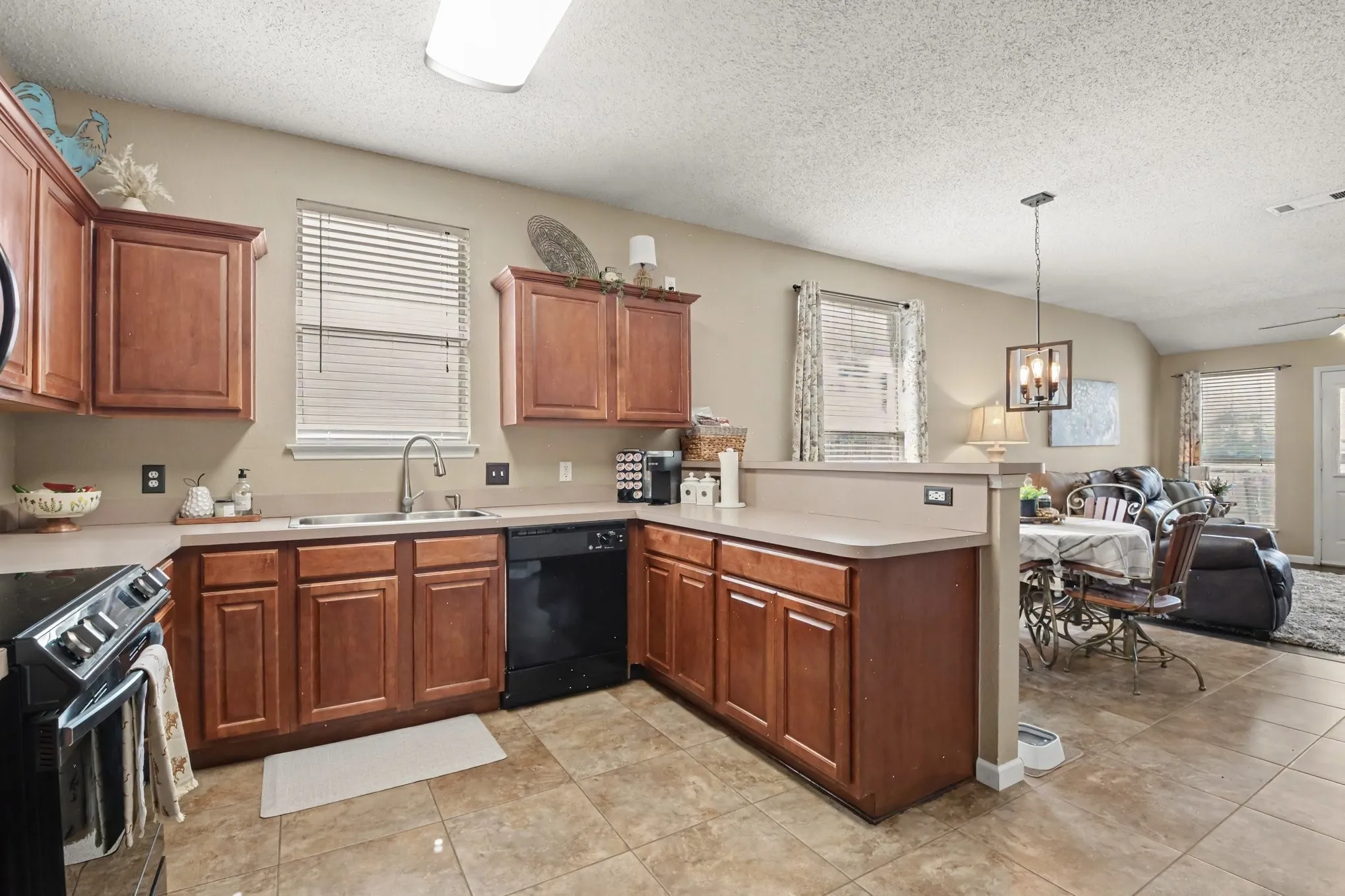 Kitchen featuring tile flooring, wood-finish cabinetry, black appliances, a double basin sink, and a breakfast bar opening to an adjacent room