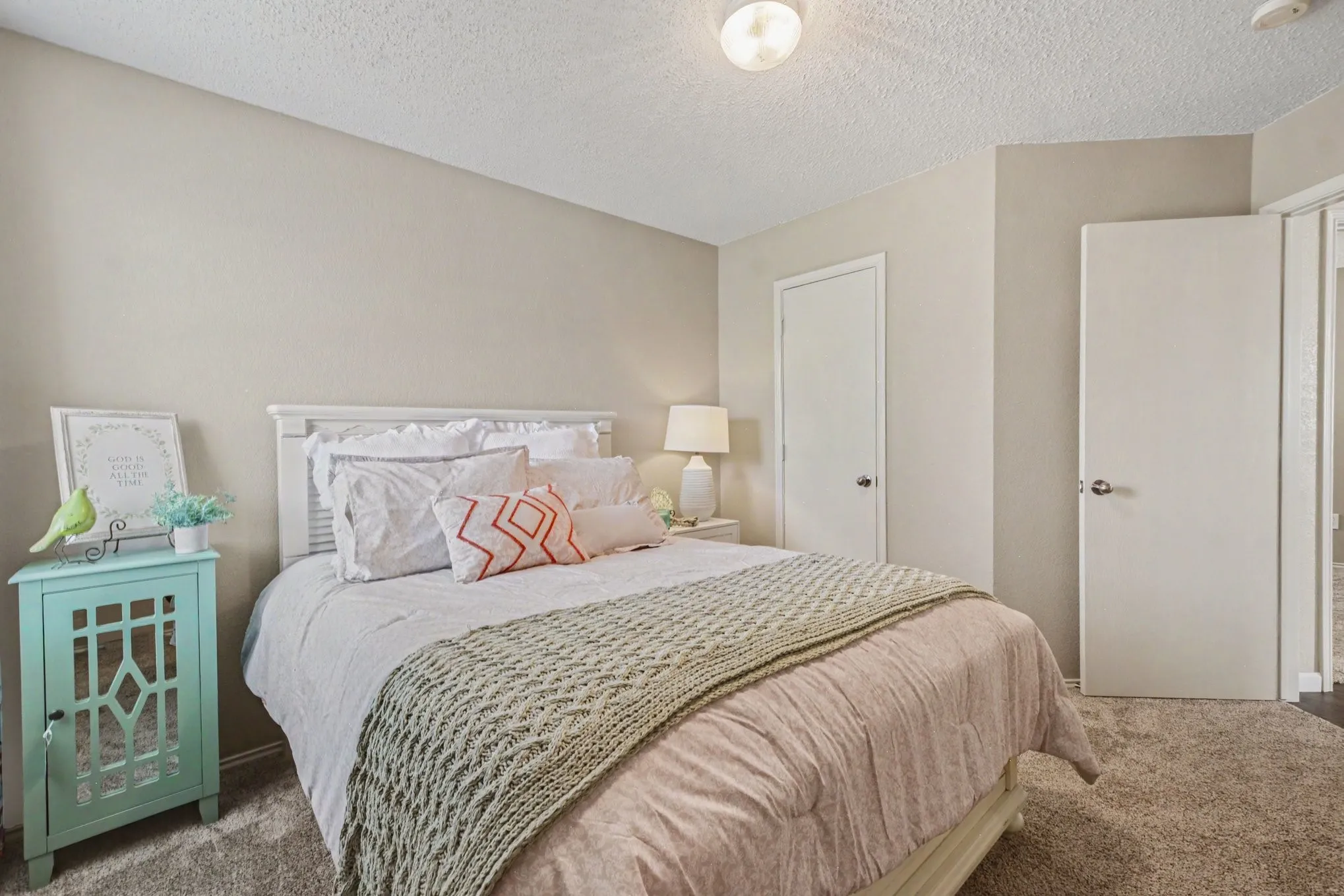 Carpeted bedroom featuring neutral-toned walls, a textured ceiling, and a white paneled door with a round knob