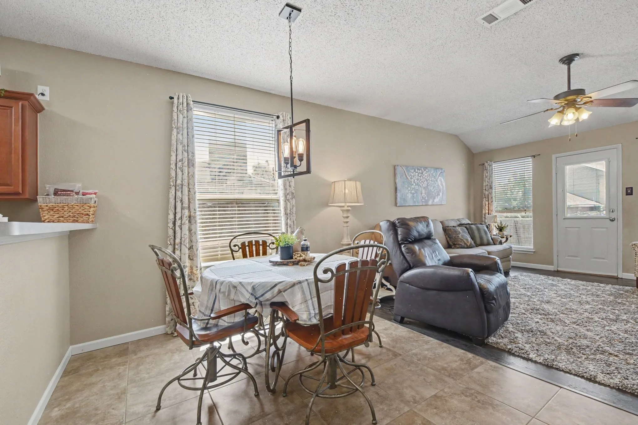 Open-concept interior featuring a breakfast area with tile flooring, a living area with wood-finish flooring, a ceiling fan, and a single exterior access door