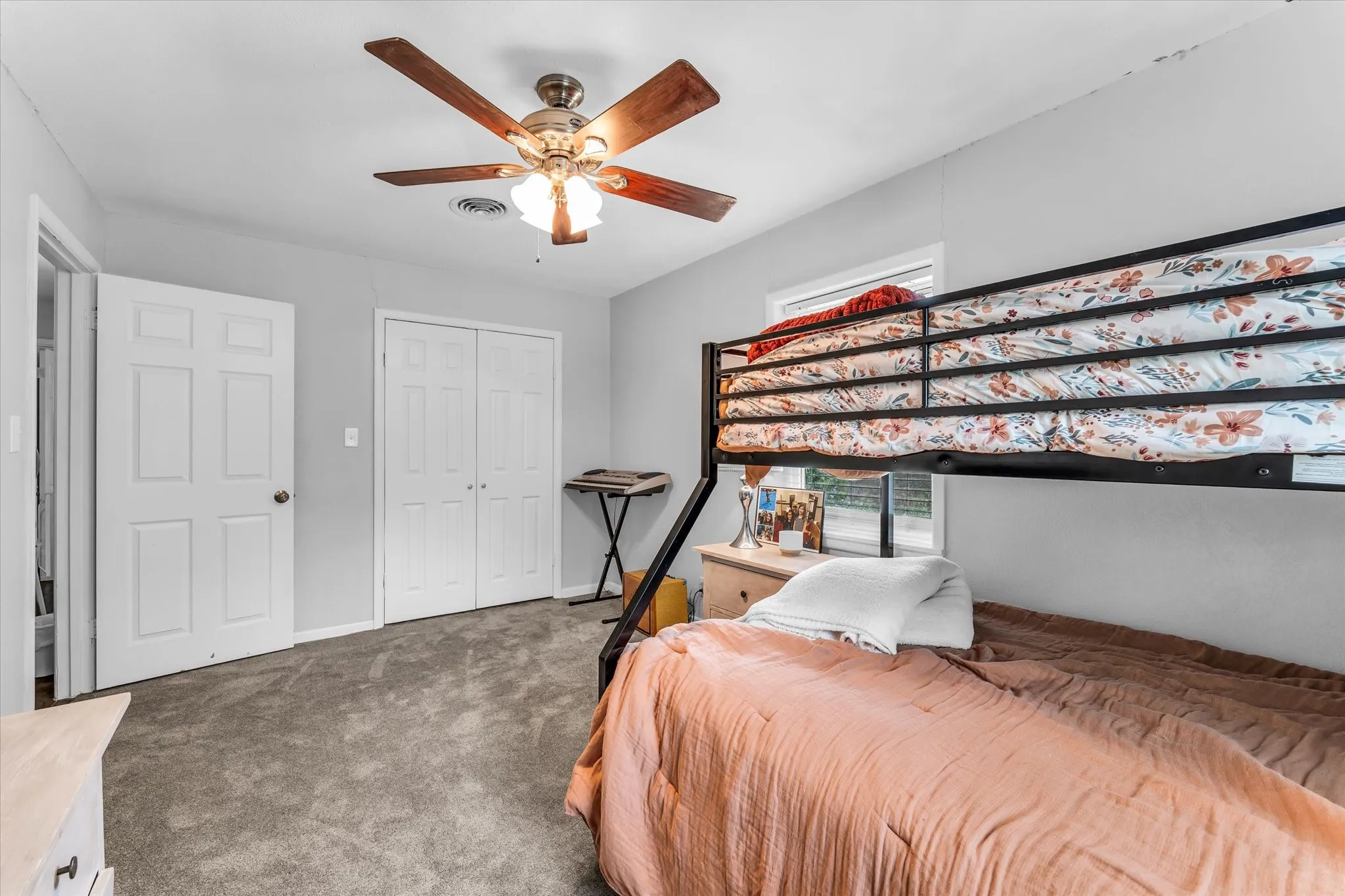 Carpeted bedroom featuring a ceiling fan with light fixture, white six-panel door, and bi-fold closet doors
