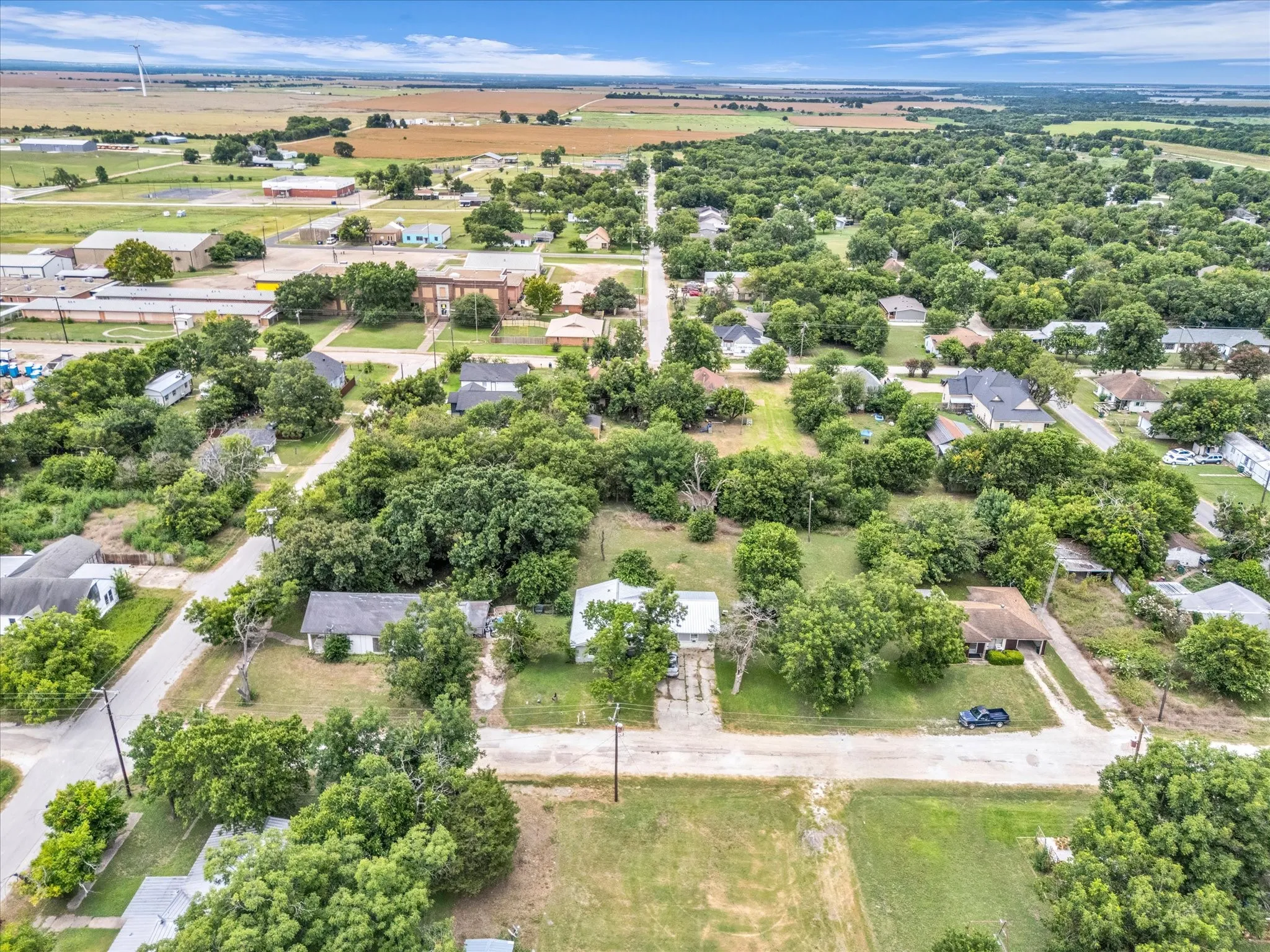 Rural setting featuring extensive tree coverage, scattered residential properties, and expansive open fields