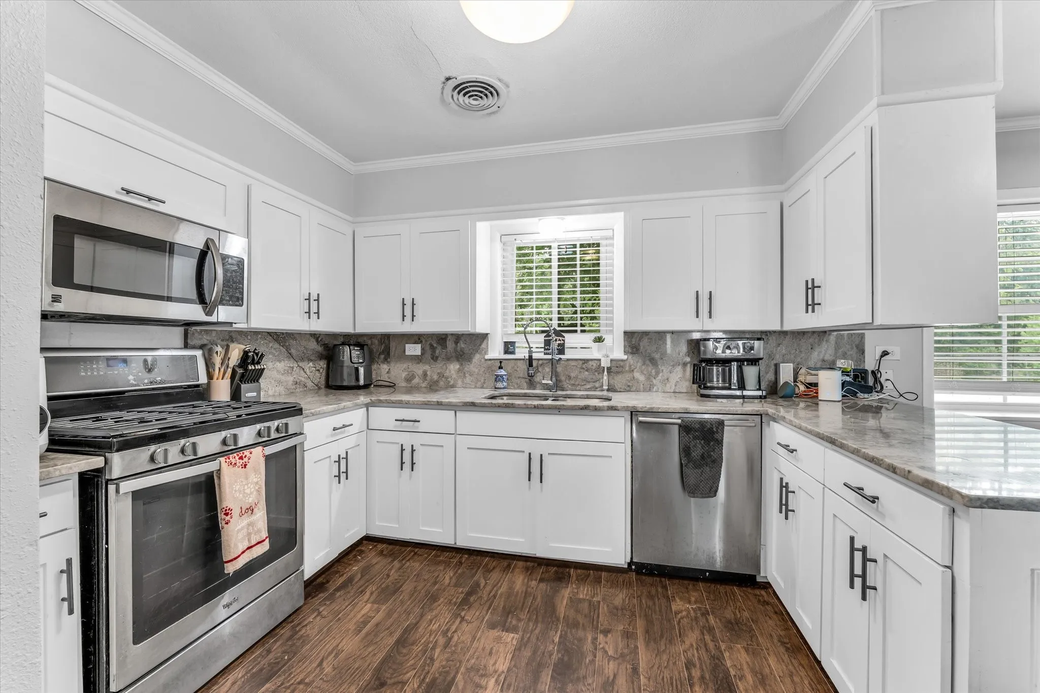 Modern kitchen featuring white shaker cabinetry, stainless steel appliances, granite countertops with a coordinating backsplash, and wood-finish flooring