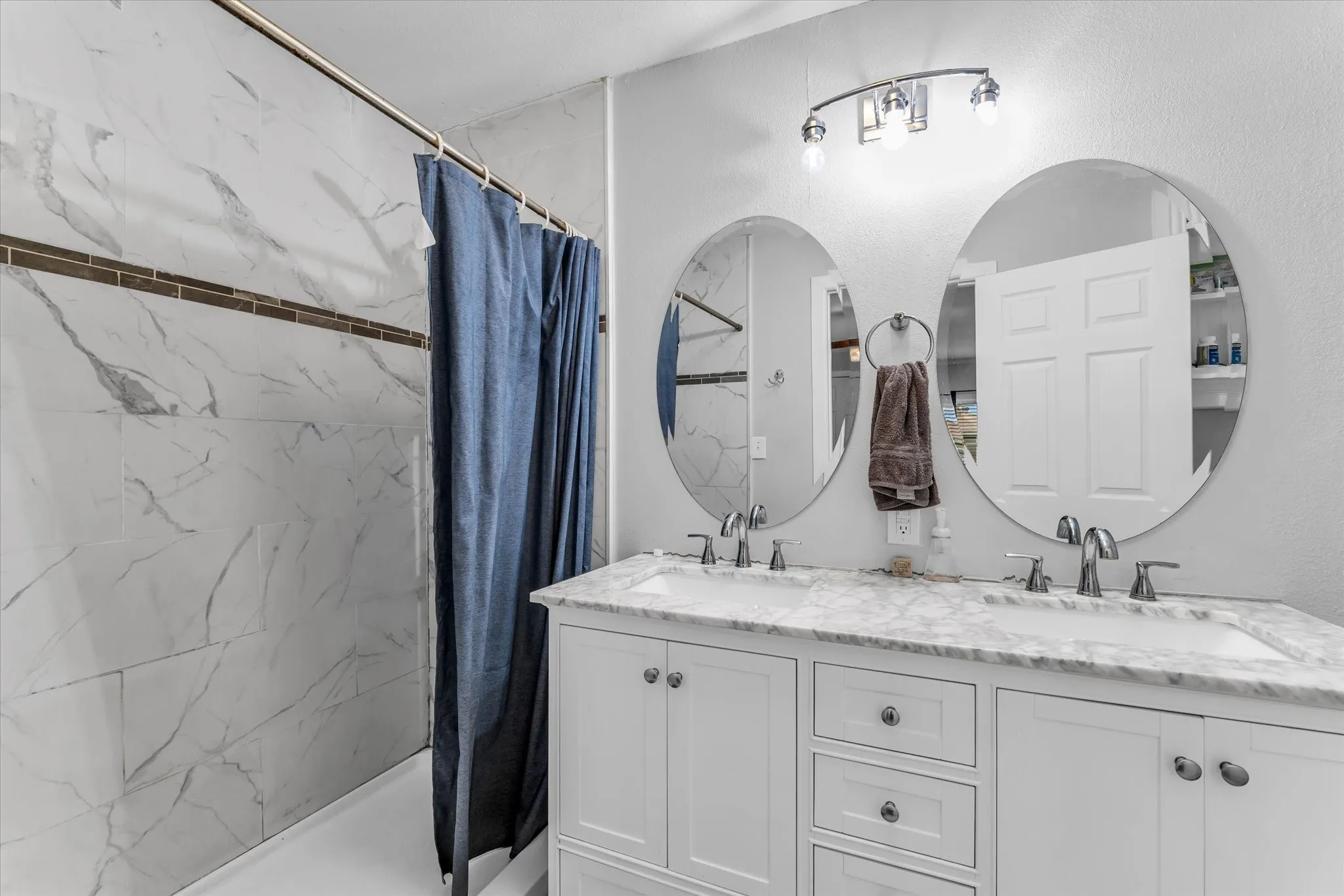 Bathroom featuring a double vanity with white cabinetry, marble-finish countertop, dual undermount sinks, and polished chrome fixtures