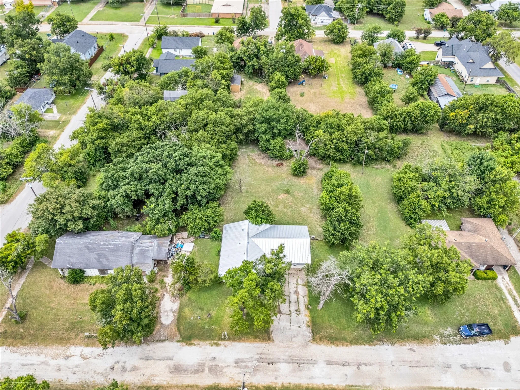Expansive lot with mature trees and significant green space, featuring a central residence with a light-colored roof