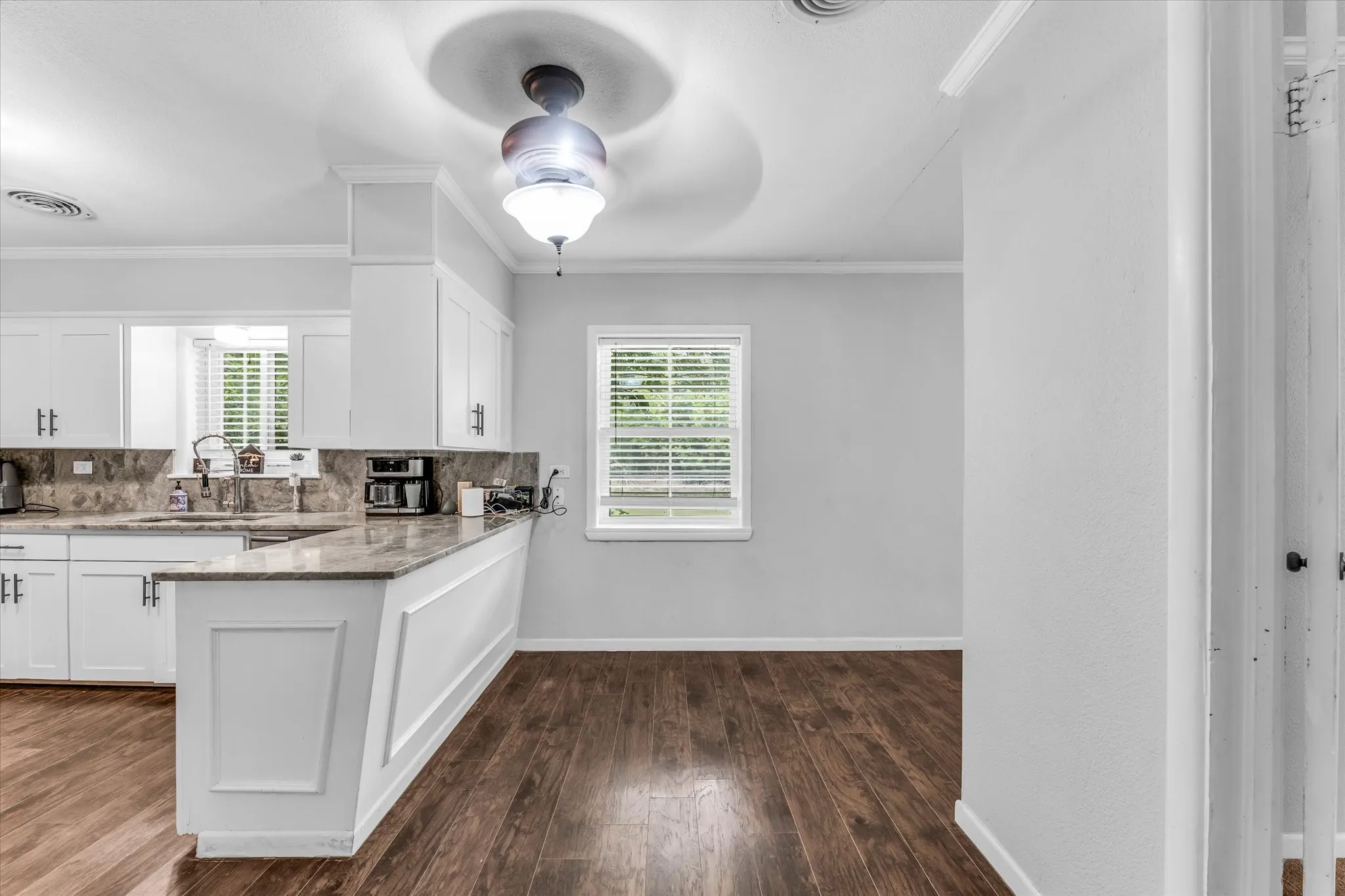 Kitchen featuring white cabinetry, a built-in sink, stone countertops and backsplash, and dark wood-finish flooring