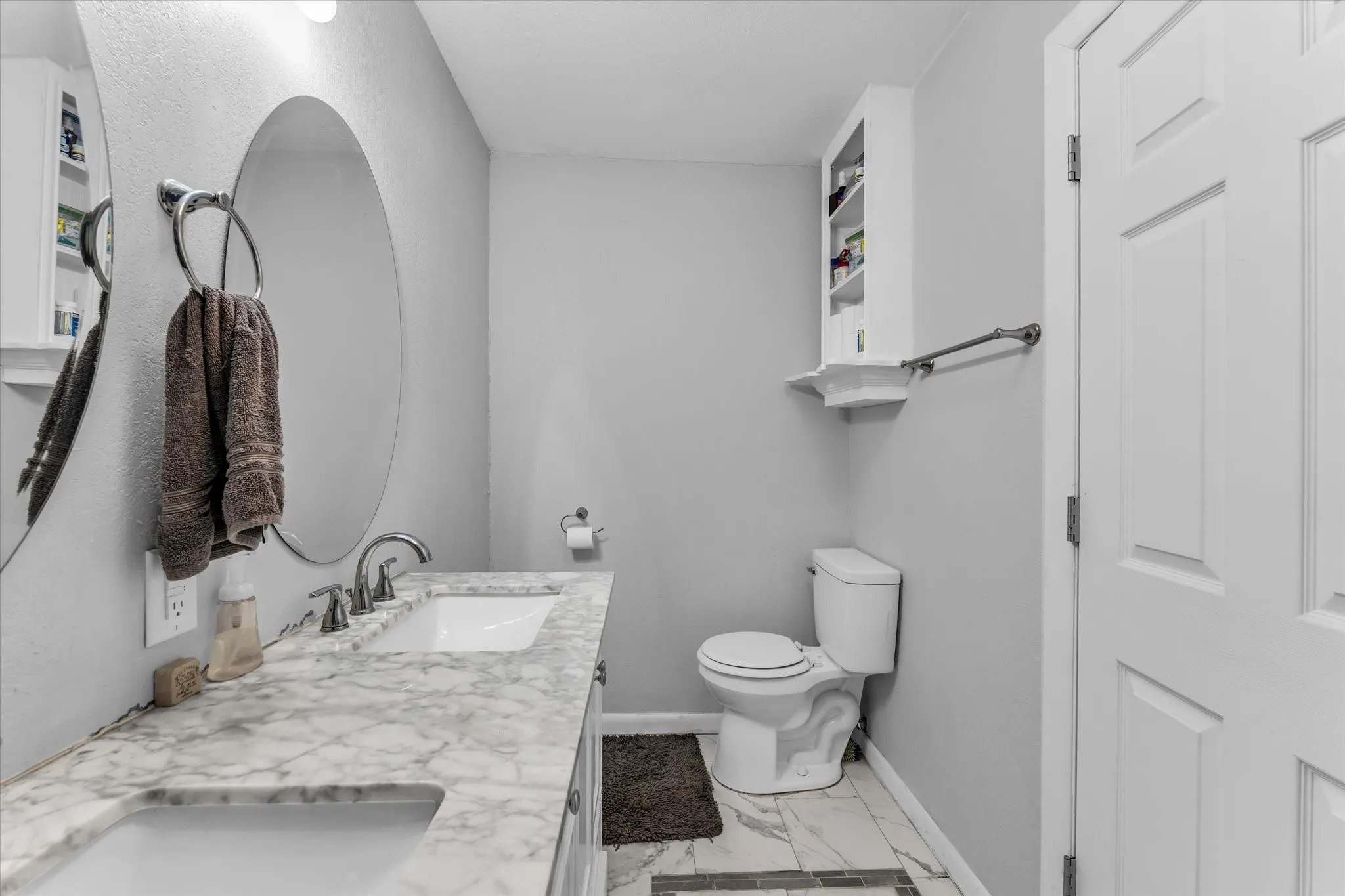 Bathroom featuring a dual-sink vanity with a marble-finish countertop, under-mount sinks, and chrome faucets