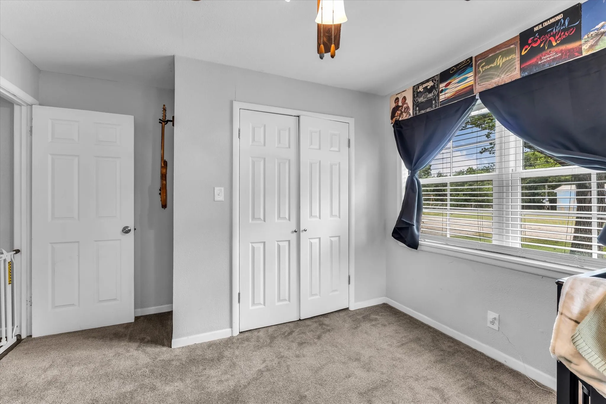 Carpeted room featuring a large window with horizontal blinds, a white six-panel door, and a double bi-fold closet door