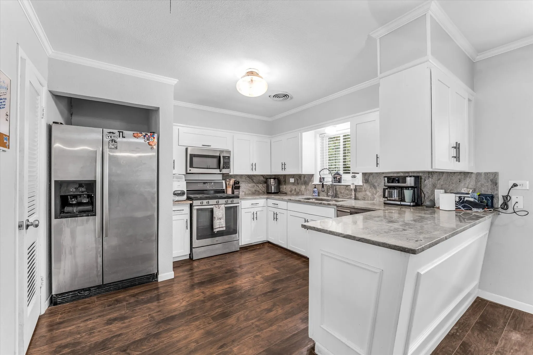 Kitchen featuring white cabinetry, stainless steel appliances, wood-finish flooring, stone countertops, and a breakfast bar