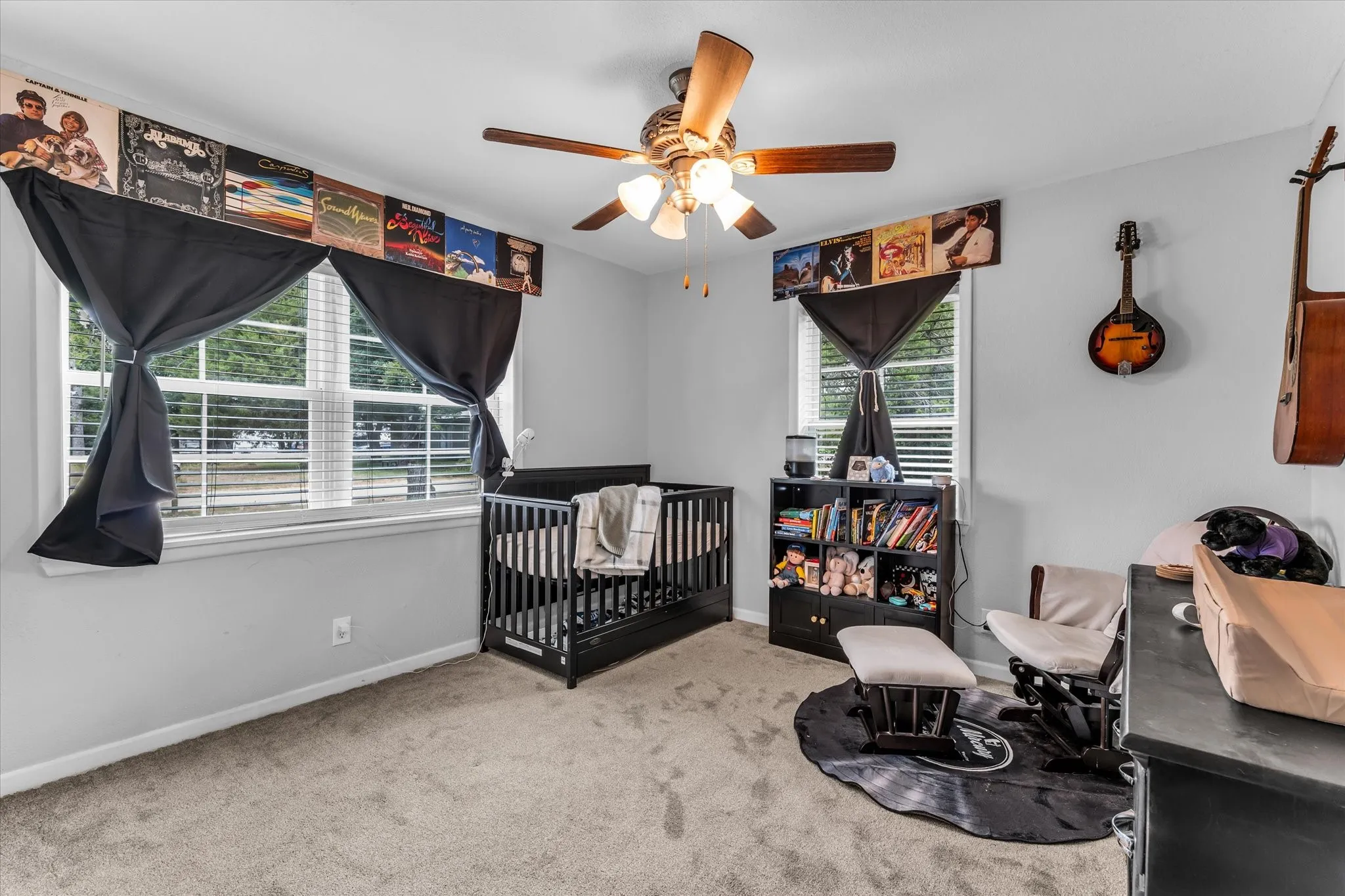 Room featuring light gray walls, carpet flooring, a ceiling fan with light fixture, and two windows with blinds