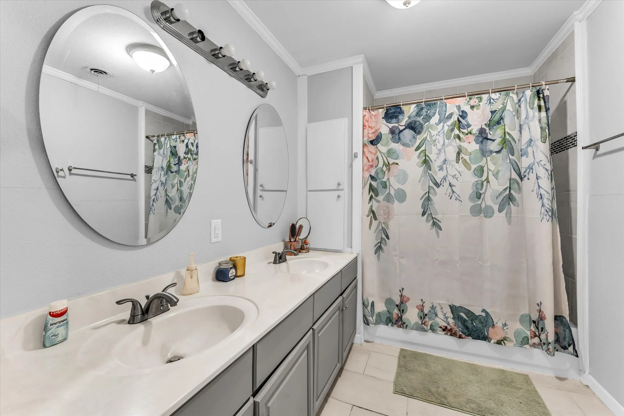 Bathroom featuring a dual vanity with undermount sinks, round frameless mirrors, and a tiled shower with a decorative accent band