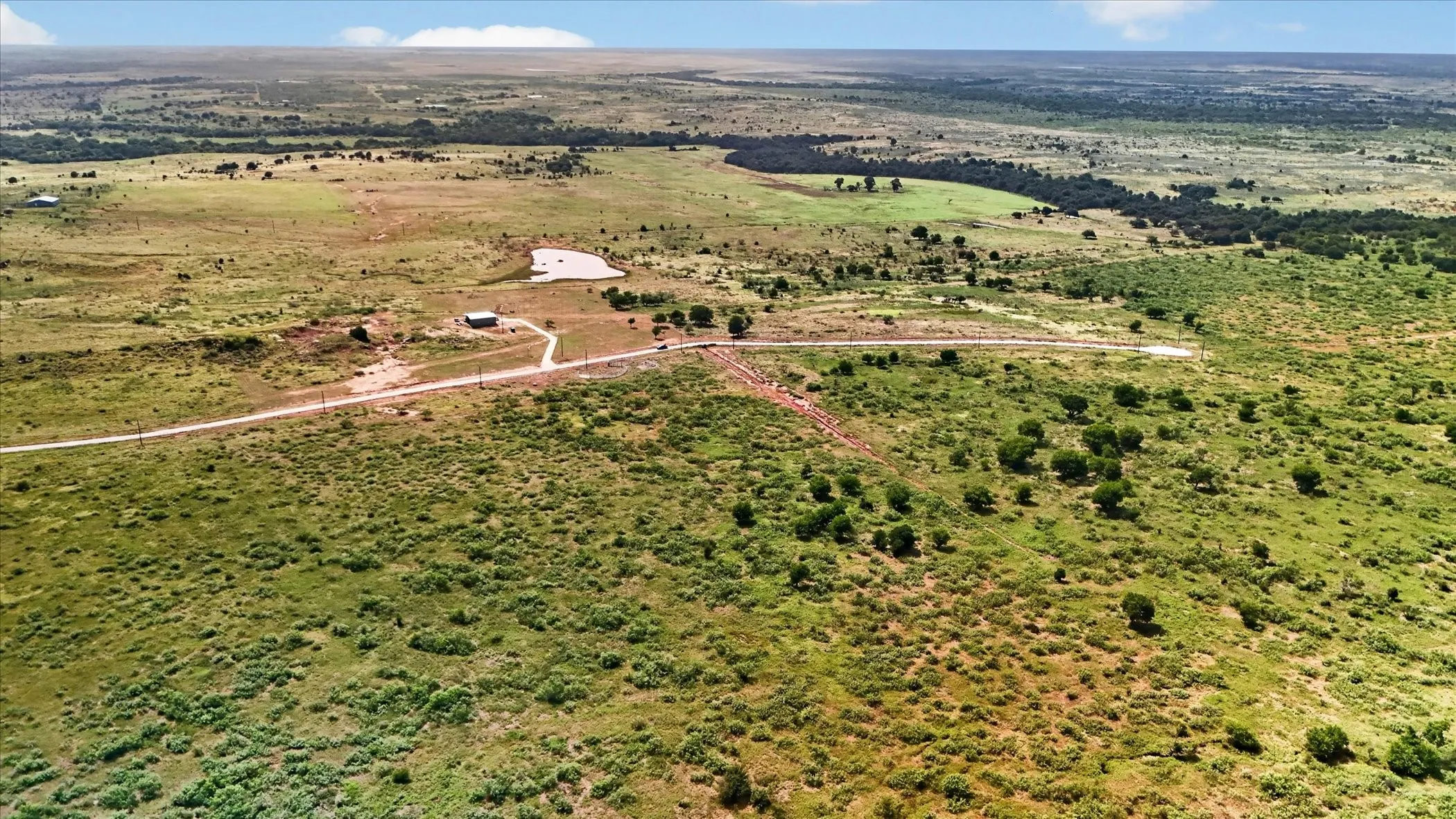 Expansive rural landscape featuring a private drive, a small building, and a natural pond