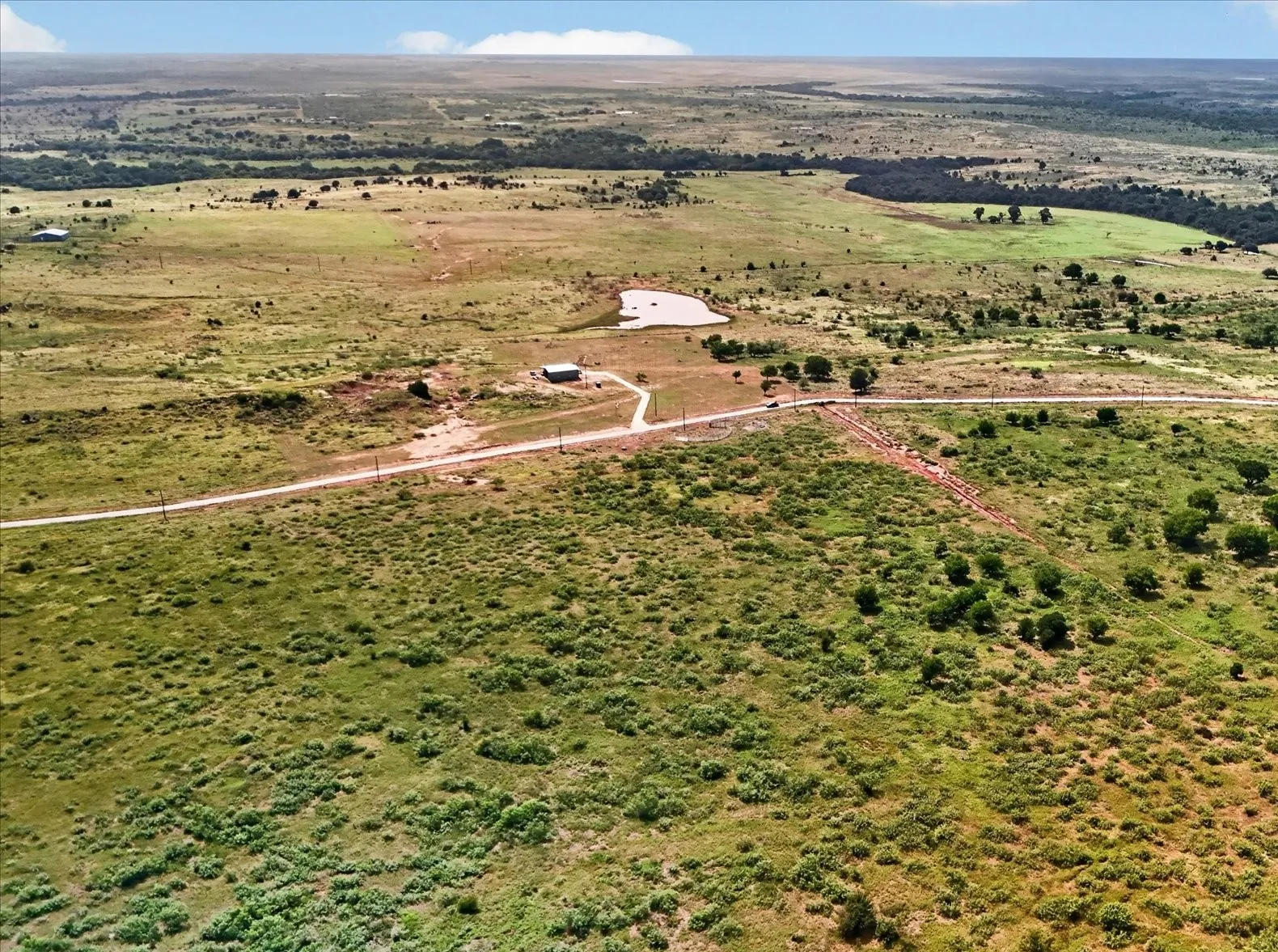 Expansive rural landscape featuring a private pond, open grasslands, scattered trees, and a visible access road