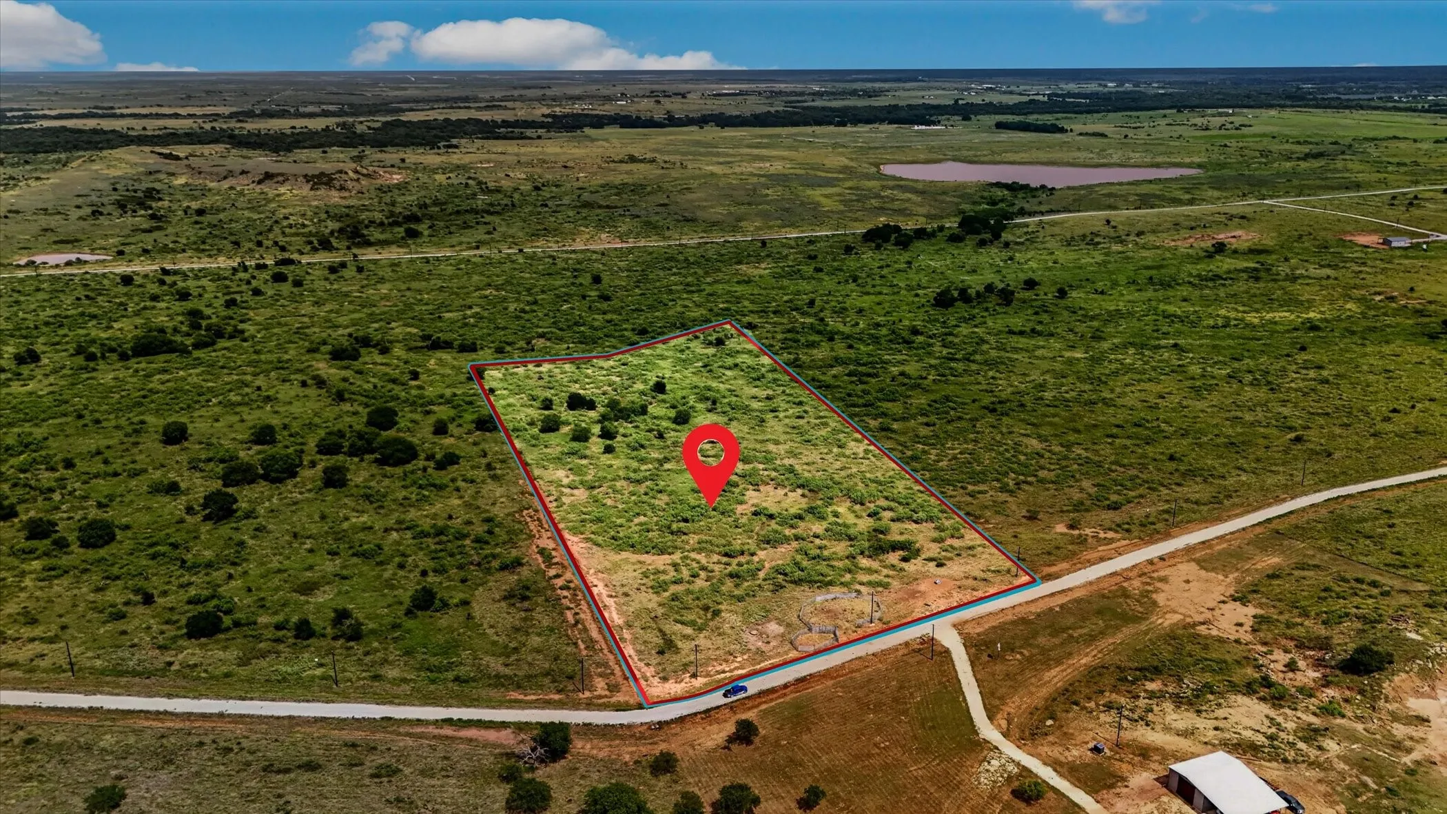 Expansive undeveloped lot featuring a red outline, surrounding natural terrain, and a visible road