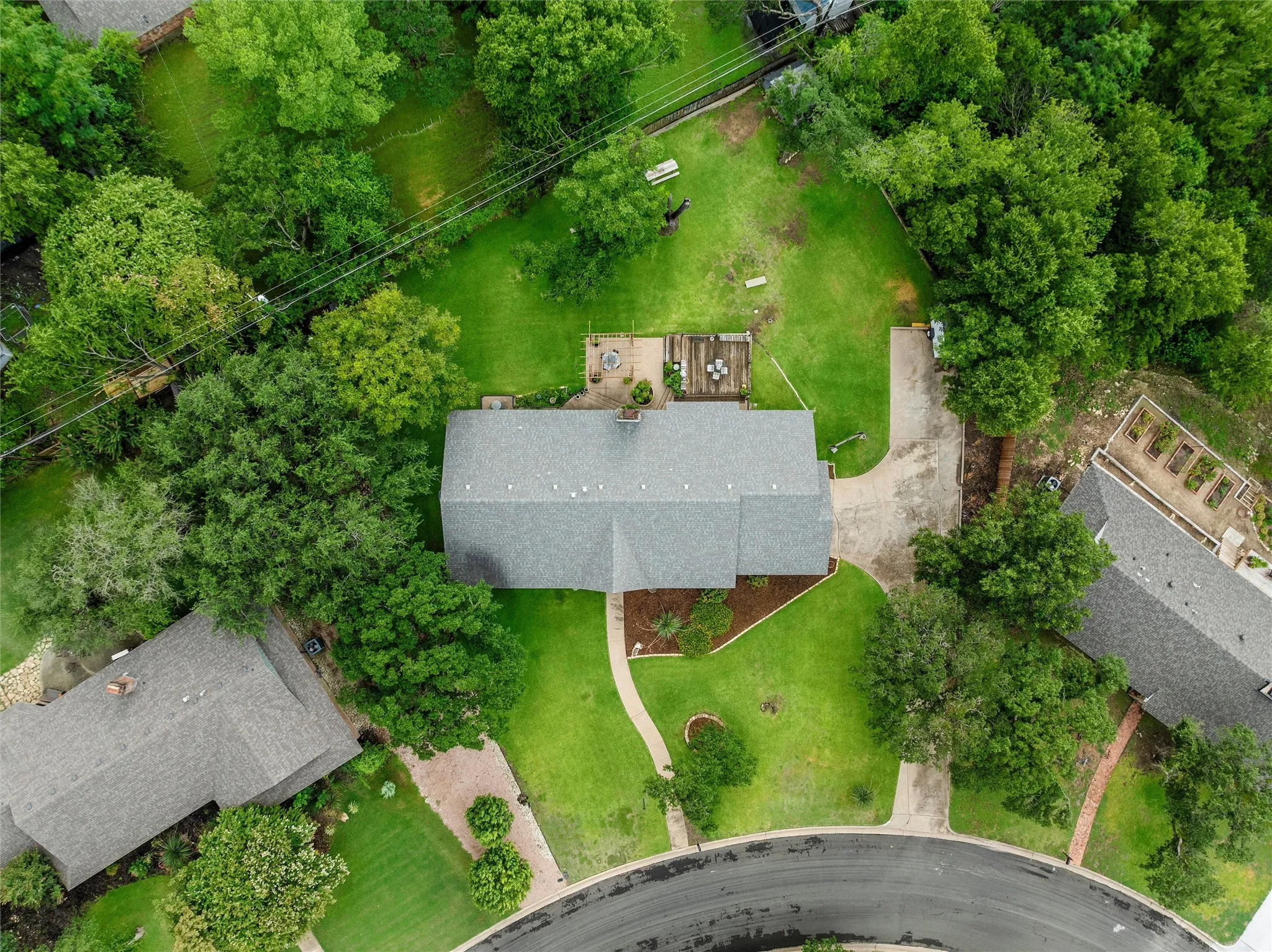 Expansive property featuring a central residence with a grey shingle roof, surrounded by mature trees and verdant lawns
