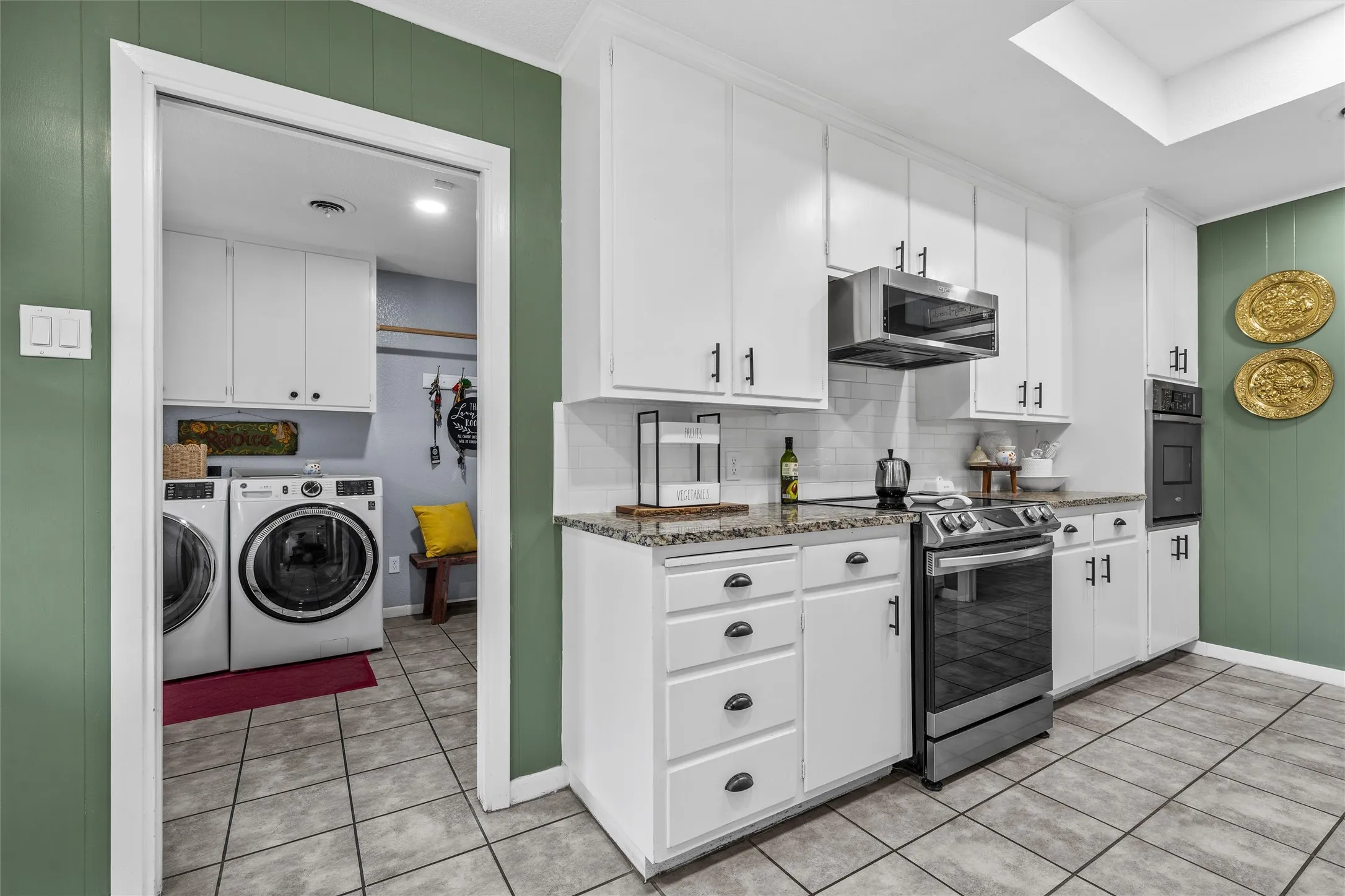 Kitchen featuring white cabinetry, stone countertops, subway tile backsplash, and stainless steel appliances, with a laundry area visible through an arched doorway