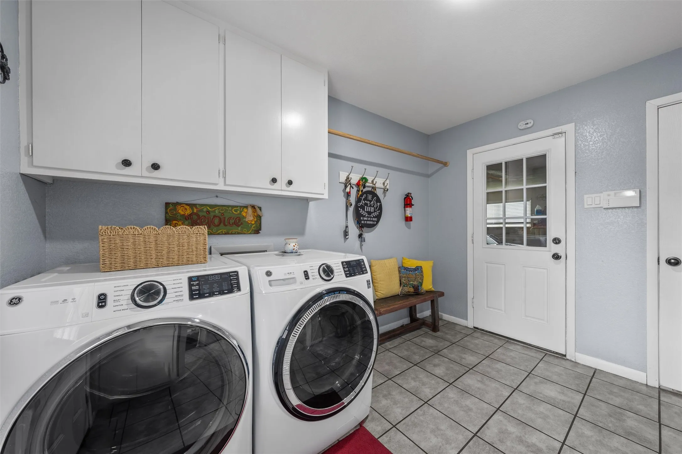 Utility room featuring durable tile flooring, white shaker-style cabinetry, and a full-light paneled exterior door