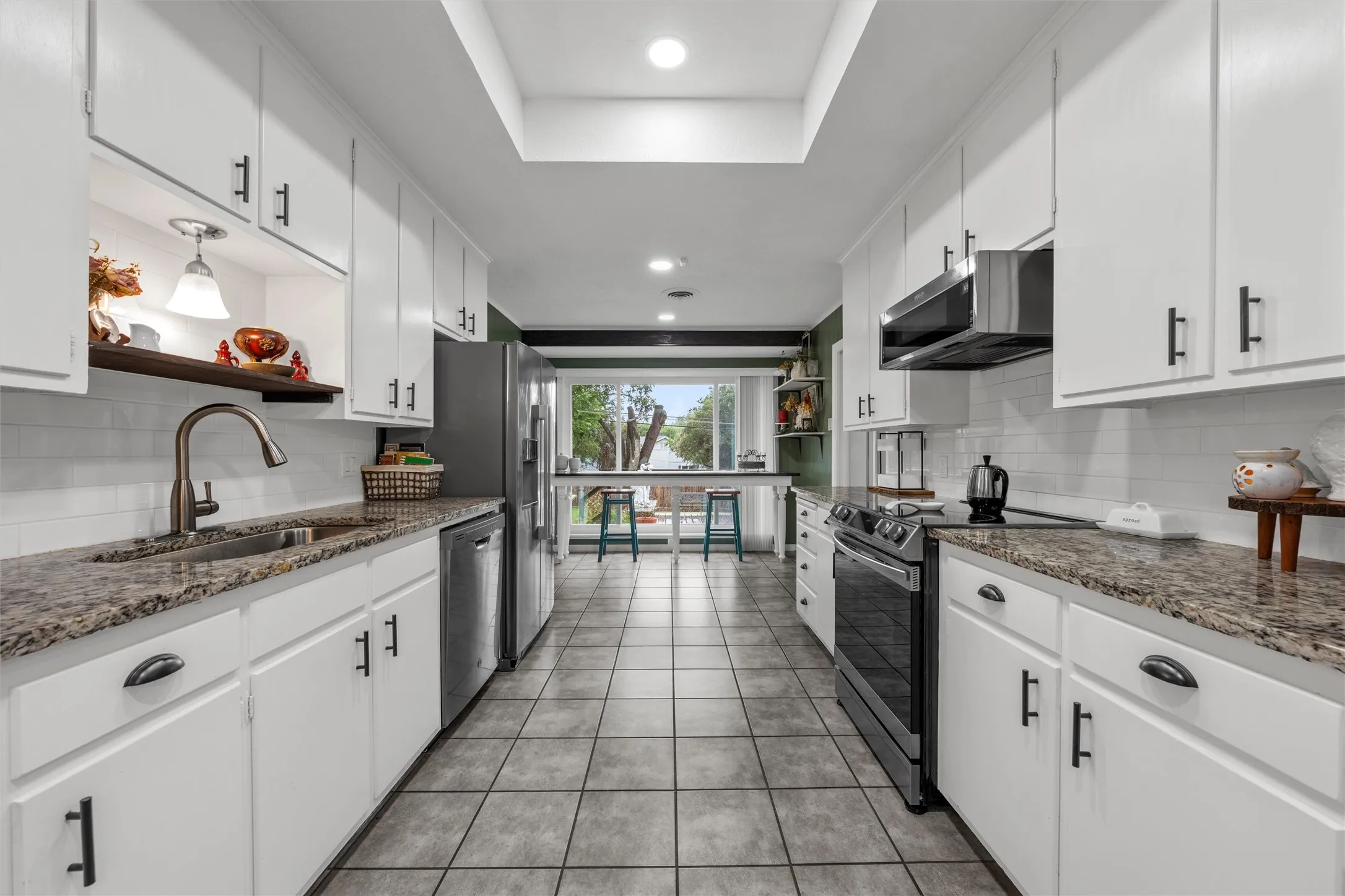 Galley kitchen featuring white cabinetry, stone-finish countertops, stainless steel appliances, a subway tile backsplash, and tile flooring