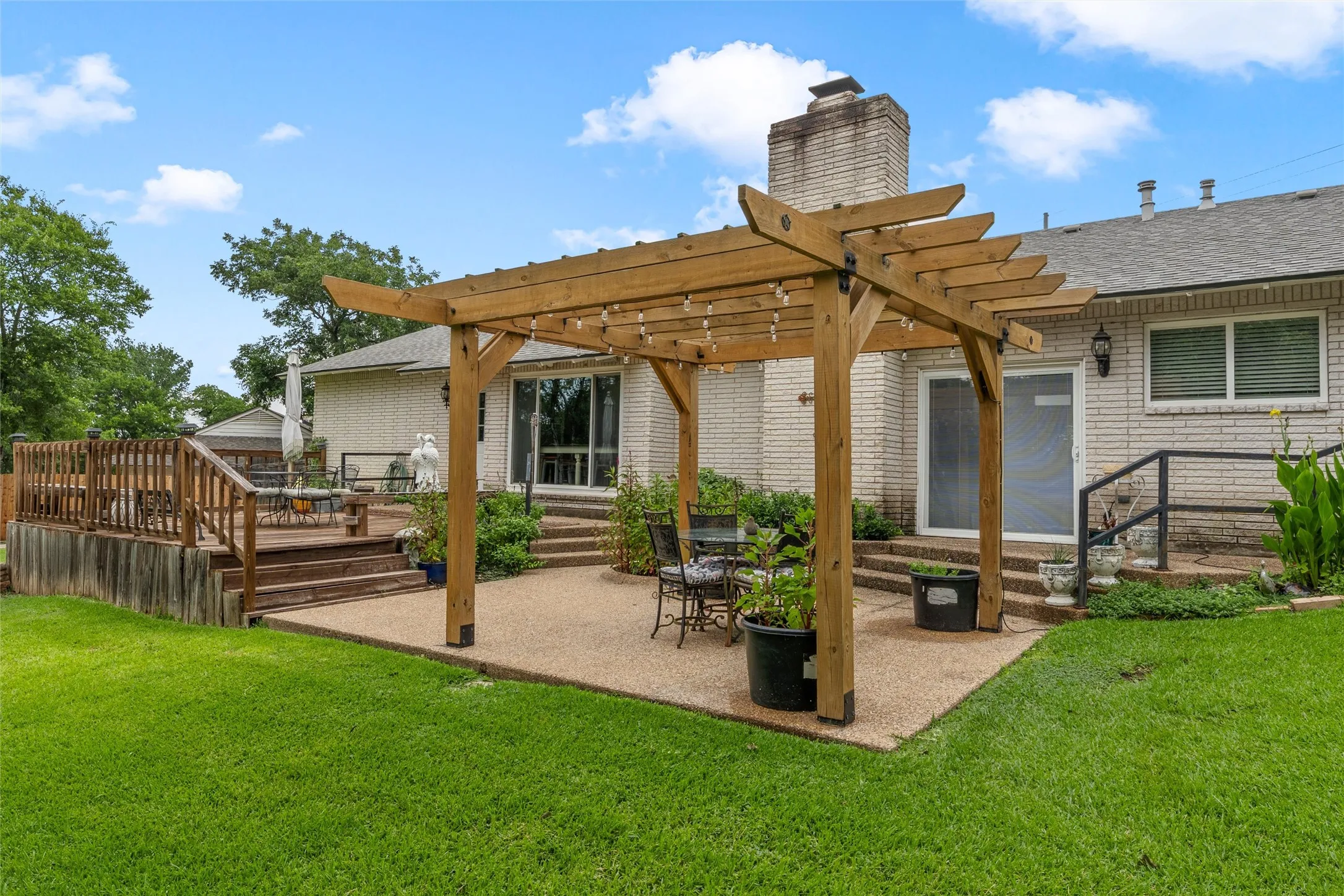 Spacious backyard featuring a wooden pergola over a concrete patio, a multi-level wood deck with railings, and a manicured lawn