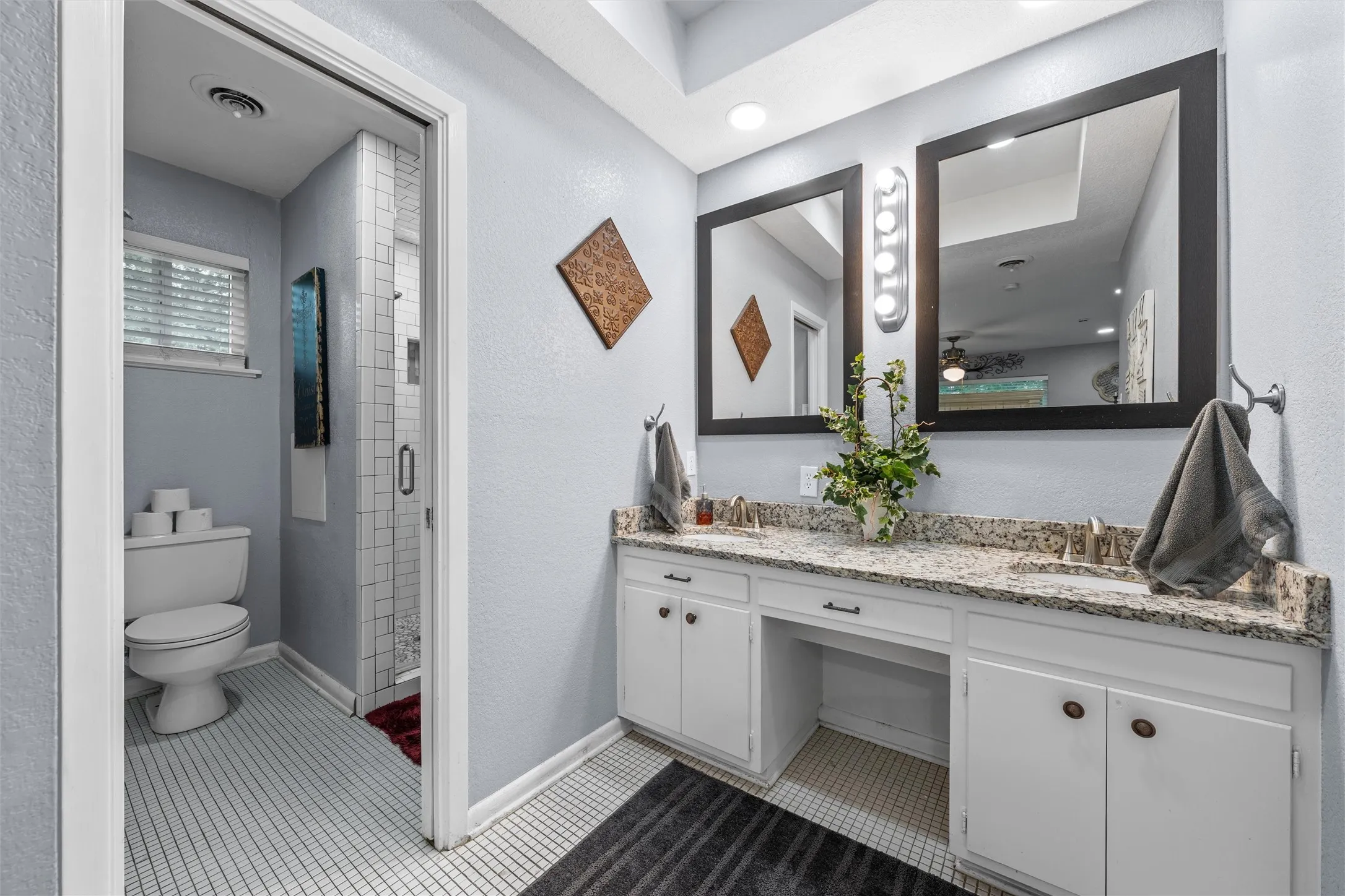 Double vanity featuring a granite countertop, integrated sinks, white cabinetry, and framed mirrors