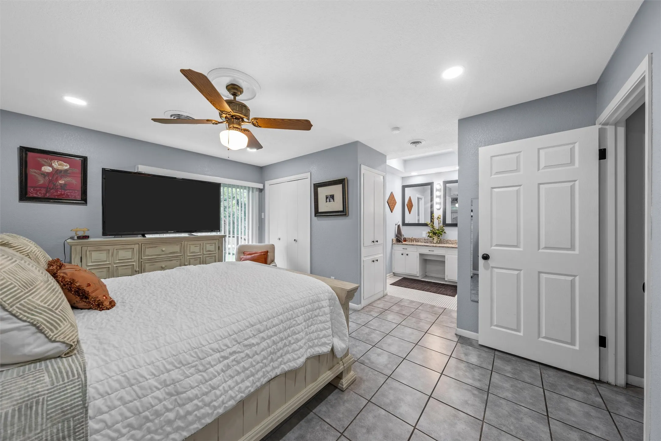 Bedroom featuring tile flooring, a ceiling fan with integrated lighting, a sliding glass door, and a private en-suite bathroom with double vanity and built-in cabinetry