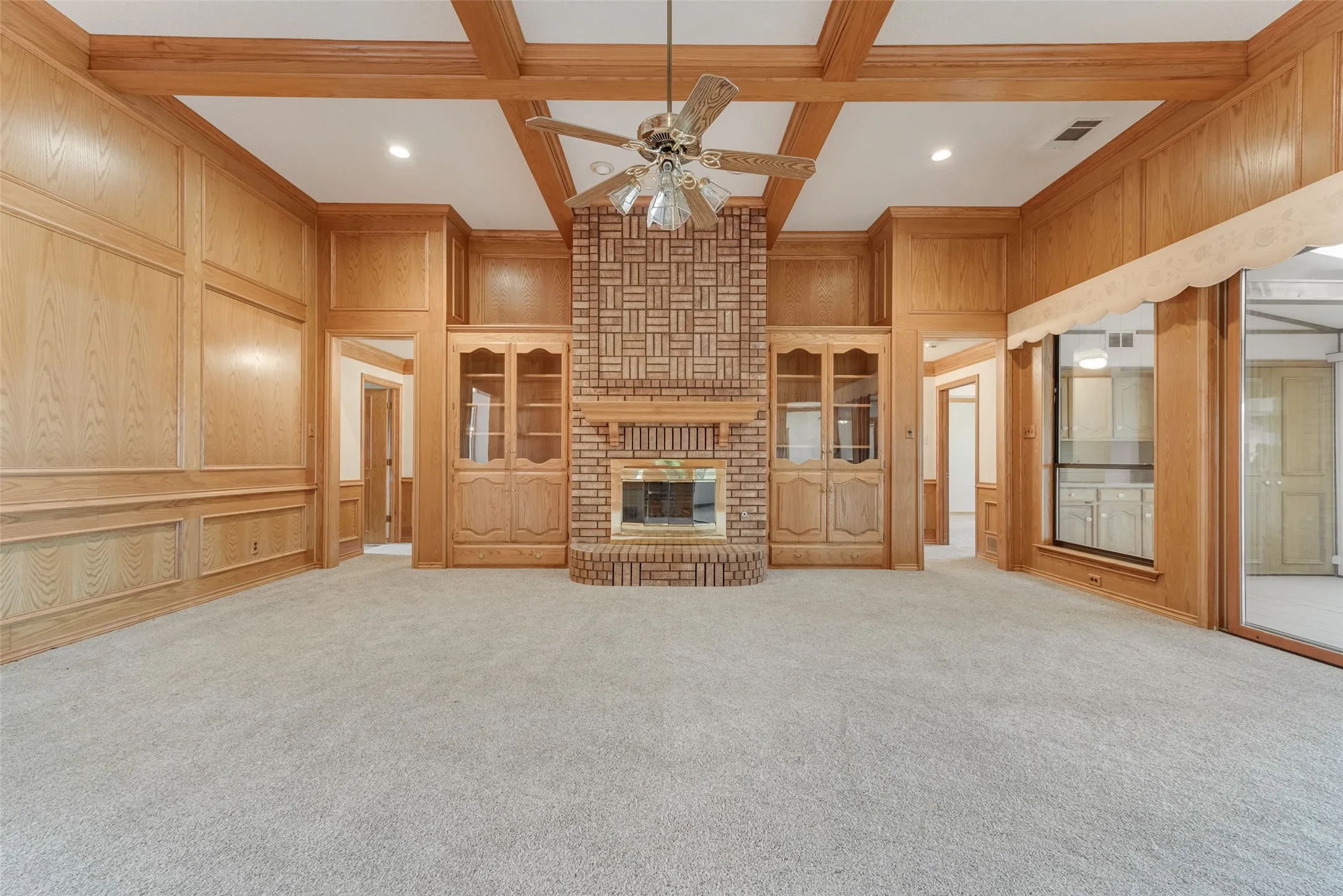 Spacious room featuring light-colored carpeting, extensive wood paneling, and a brick fireplace