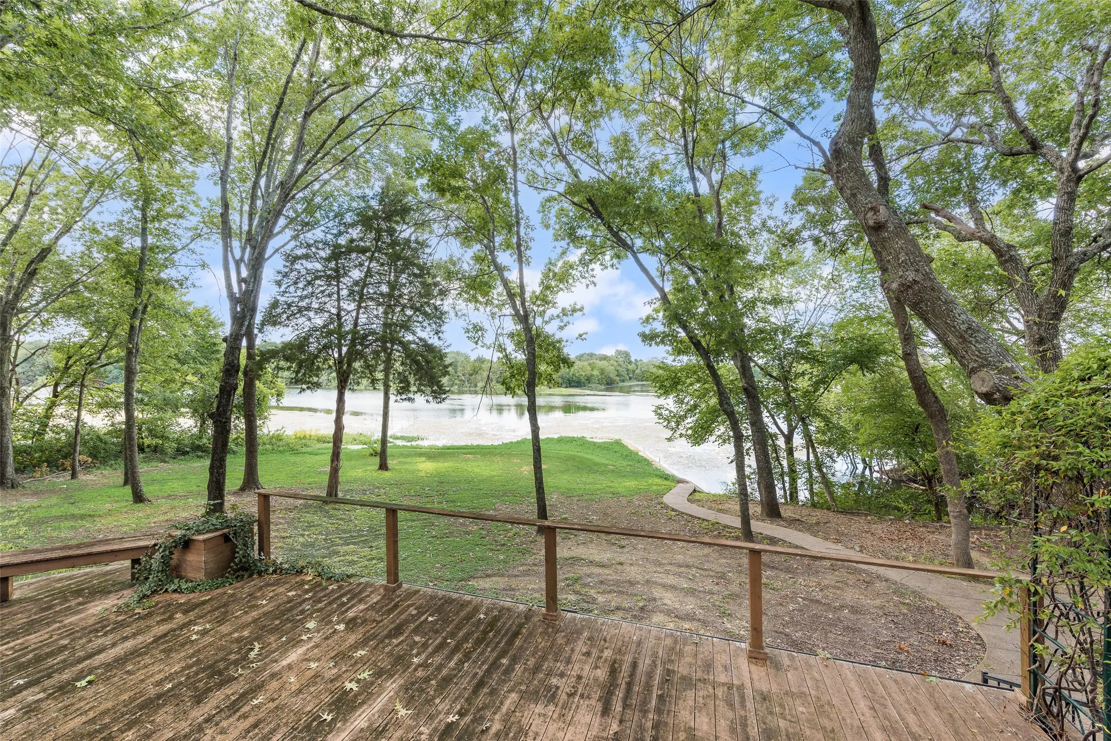 Expansive wood-finish deck overlooking a body of water, bordered by mature trees