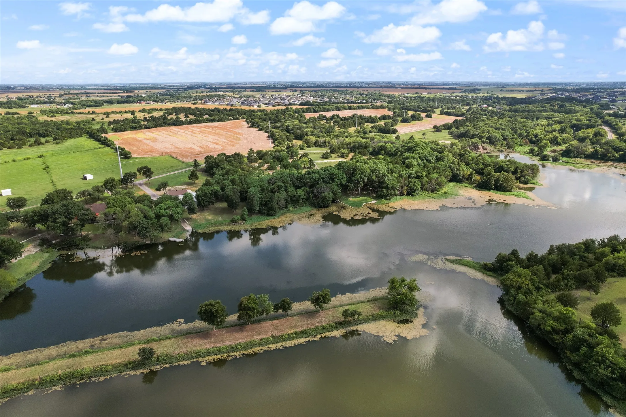 Expansive lakefront property featuring a private boat dock, extensive tree coverage, cultivated fields, and open green pastures