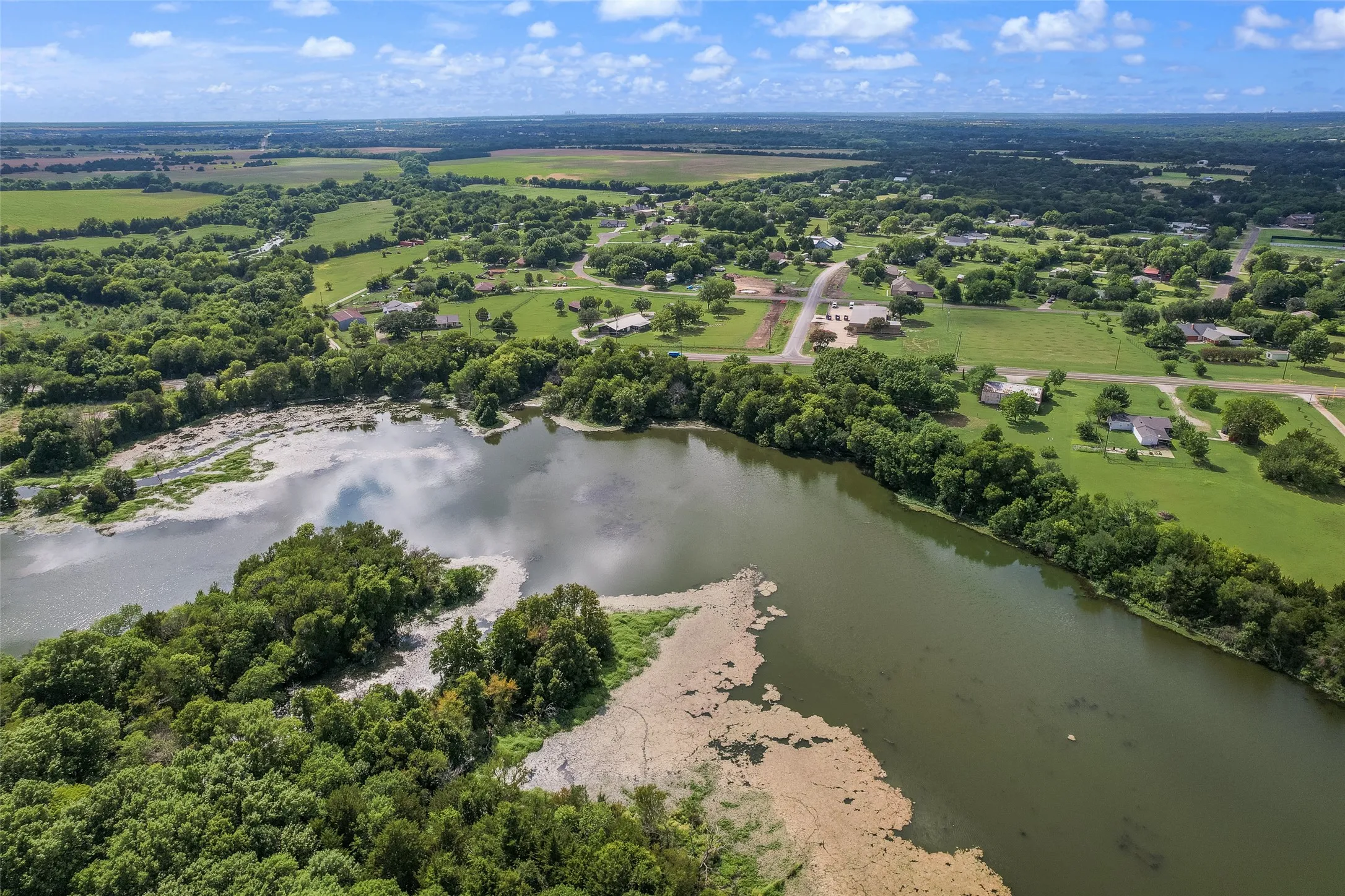 Expansive aerial panorama showcasing a large body of water, surrounded by lush green foliage and scattered residential properties