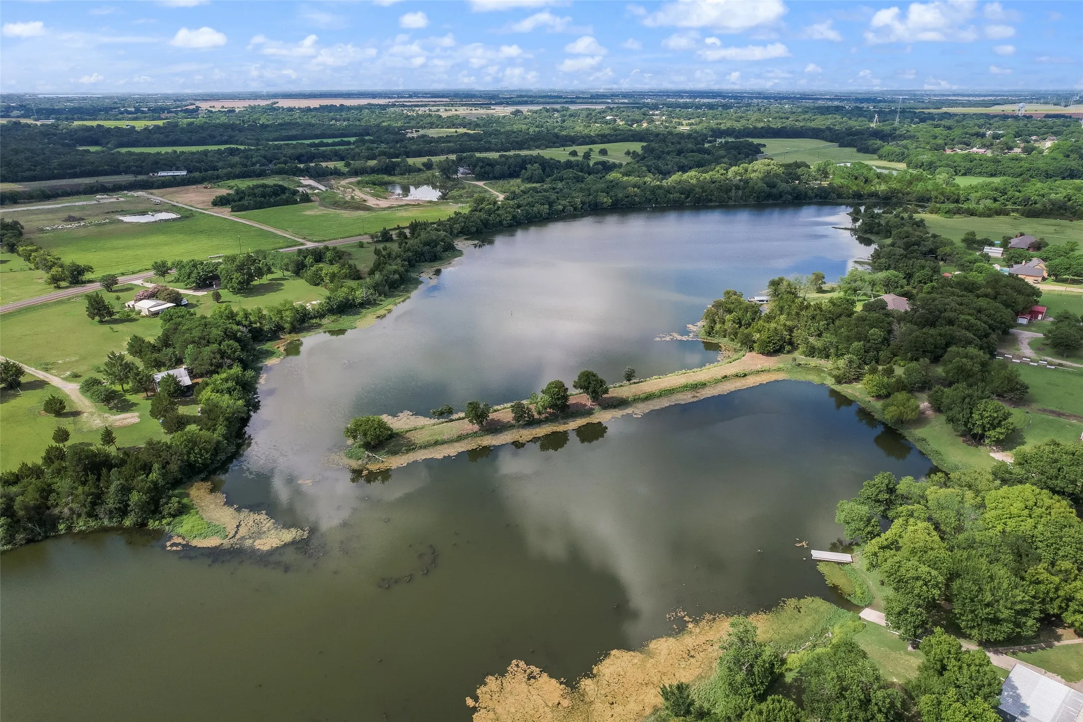 Expansive waterfront property featuring a large lake, surrounding green fields, and mature trees
