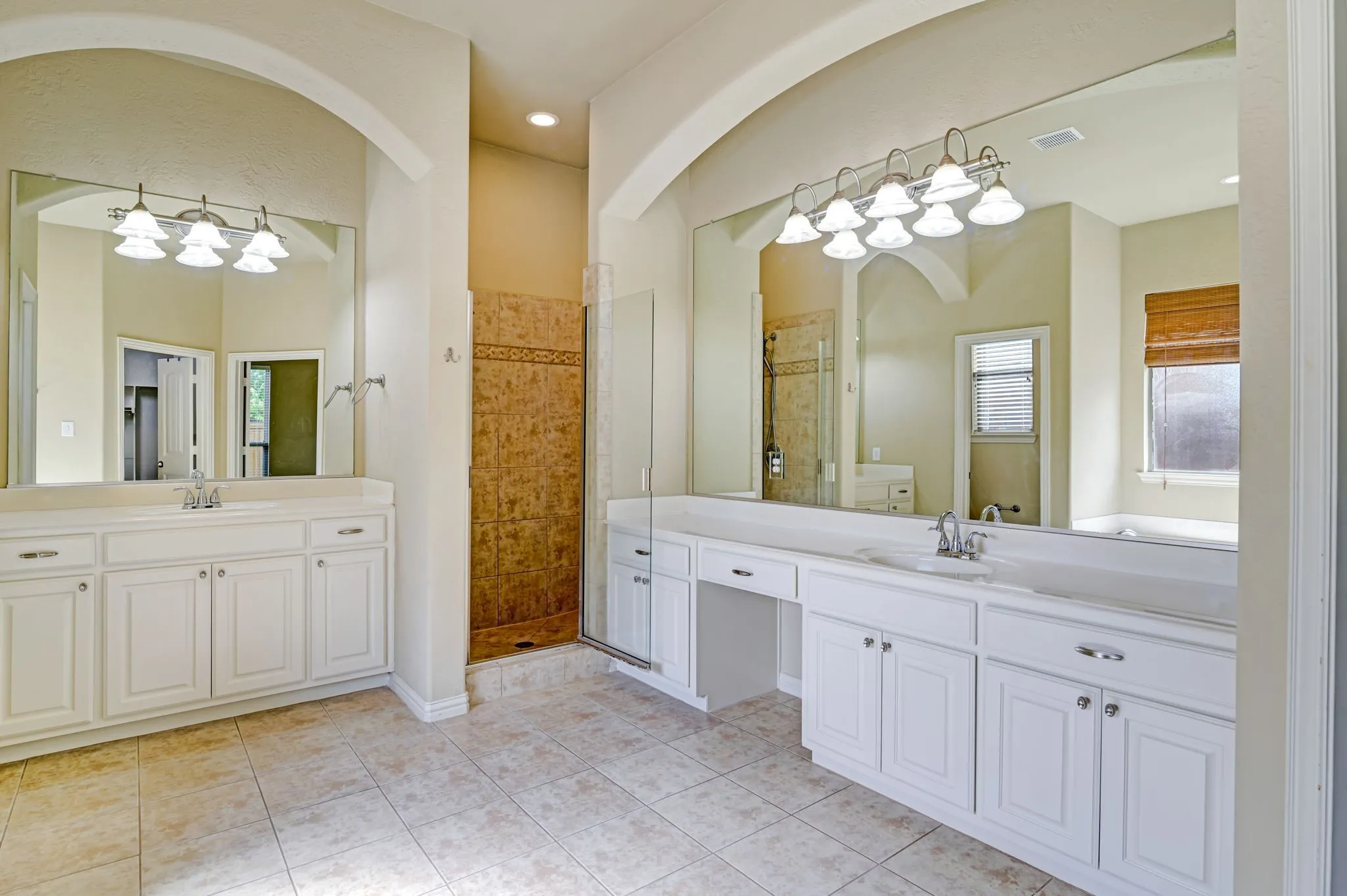 Spacious bathroom featuring dual vanities with white cabinetry, a walk-in shower with decorative tile, an integrated bathtub, and large mirrors with vanity lighting