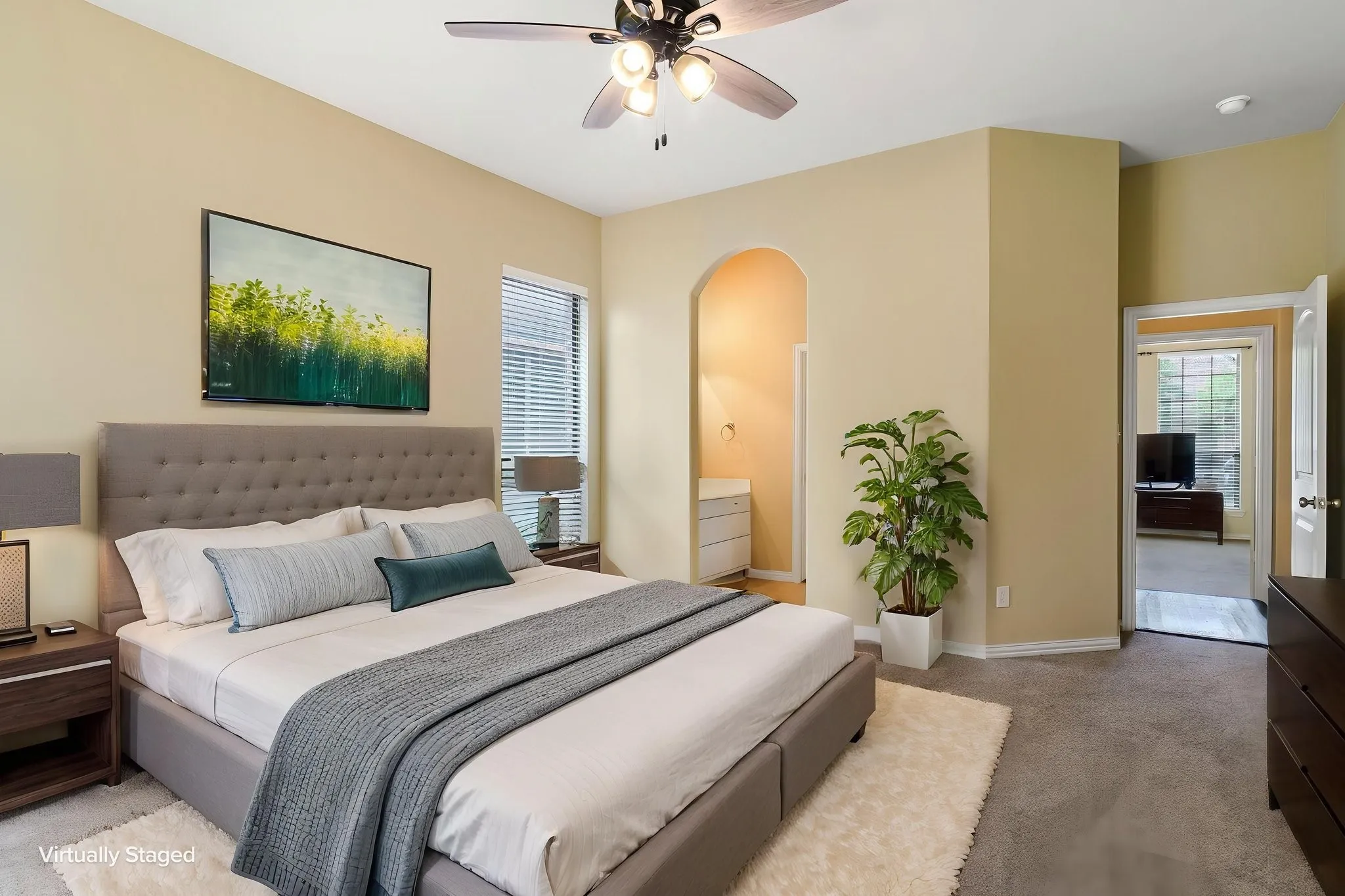 Carpeted room featuring a ceiling fan with integrated lighting, a window with horizontal blinds, an arched doorway, and an additional doorway leading to another room with wood-finish flooring