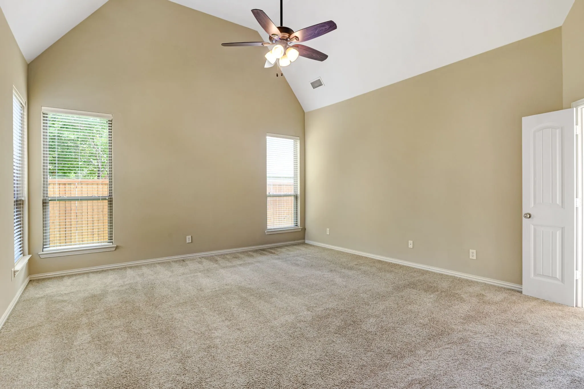 Spacious room featuring vaulted ceilings, a ceiling fan with integrated lighting, neutral-toned carpeting, and multiple windows with blinds