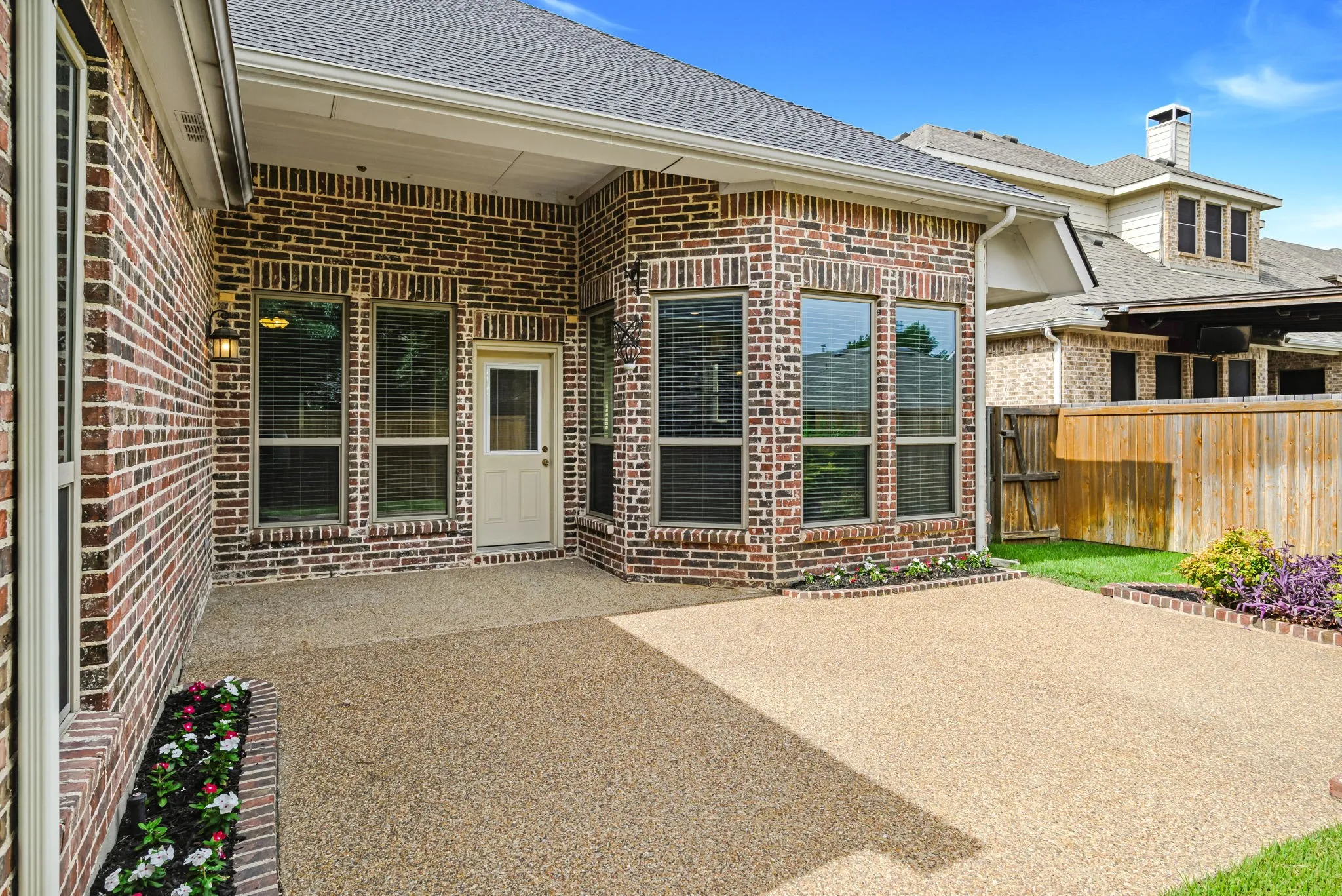 Covered outdoor patio with exposed aggregate concrete flooring, brick exterior, and multiple windows with blinds
