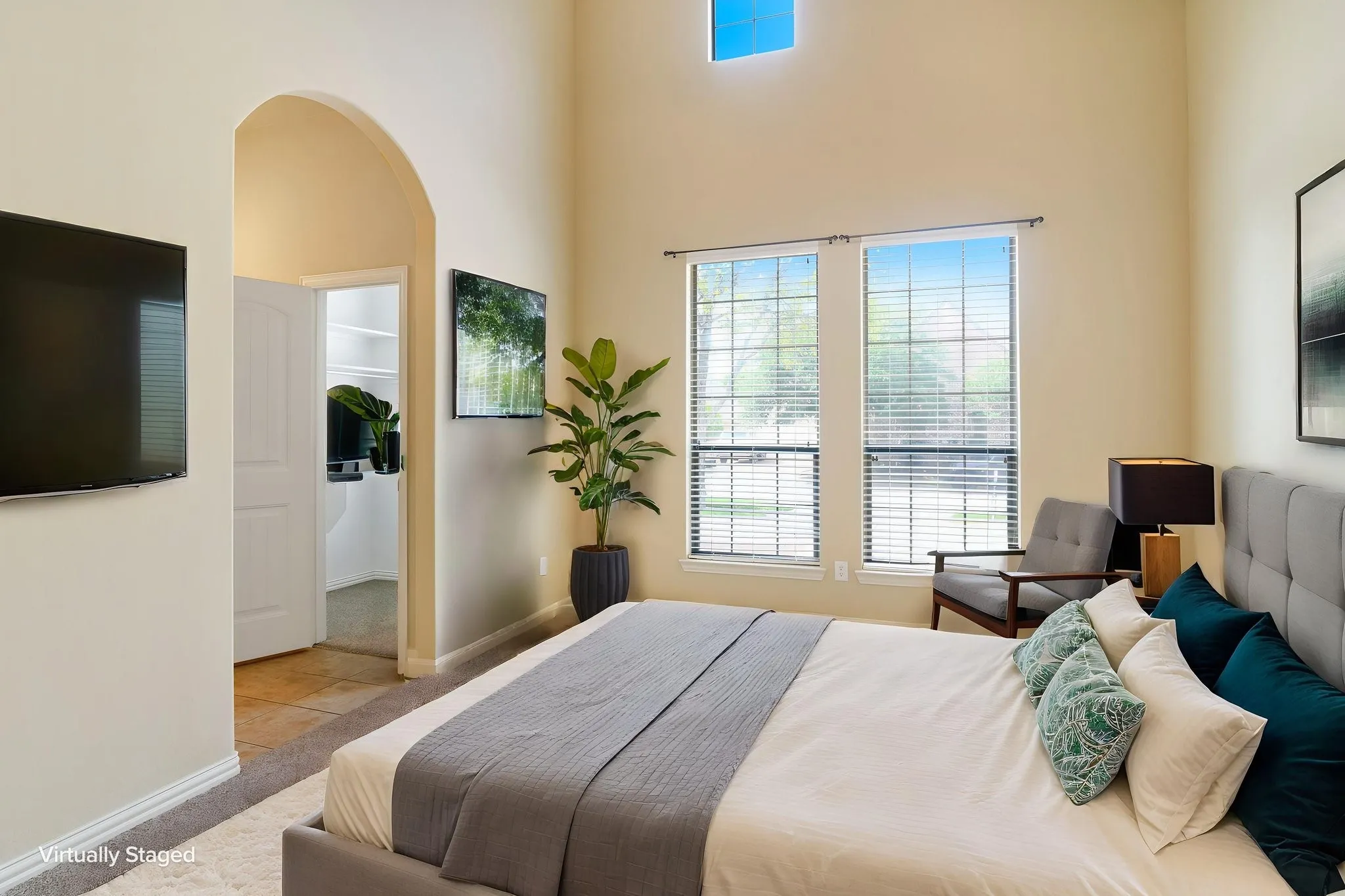 Vaulted ceiling bedroom featuring a high transom window and two large windows with blinds