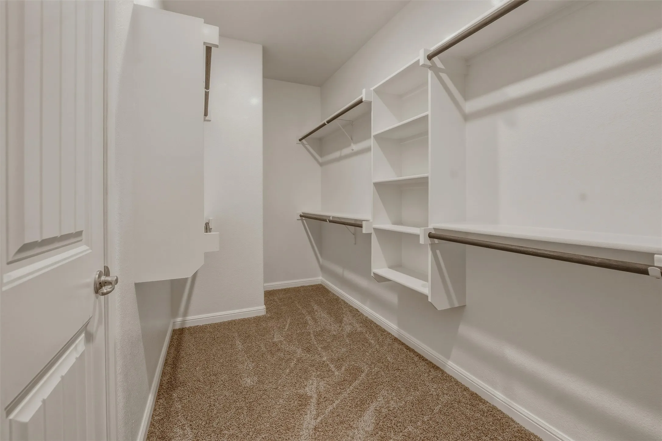 Walk-in closet featuring built-in shelving, multiple hanging rods, and neutral-toned carpeting