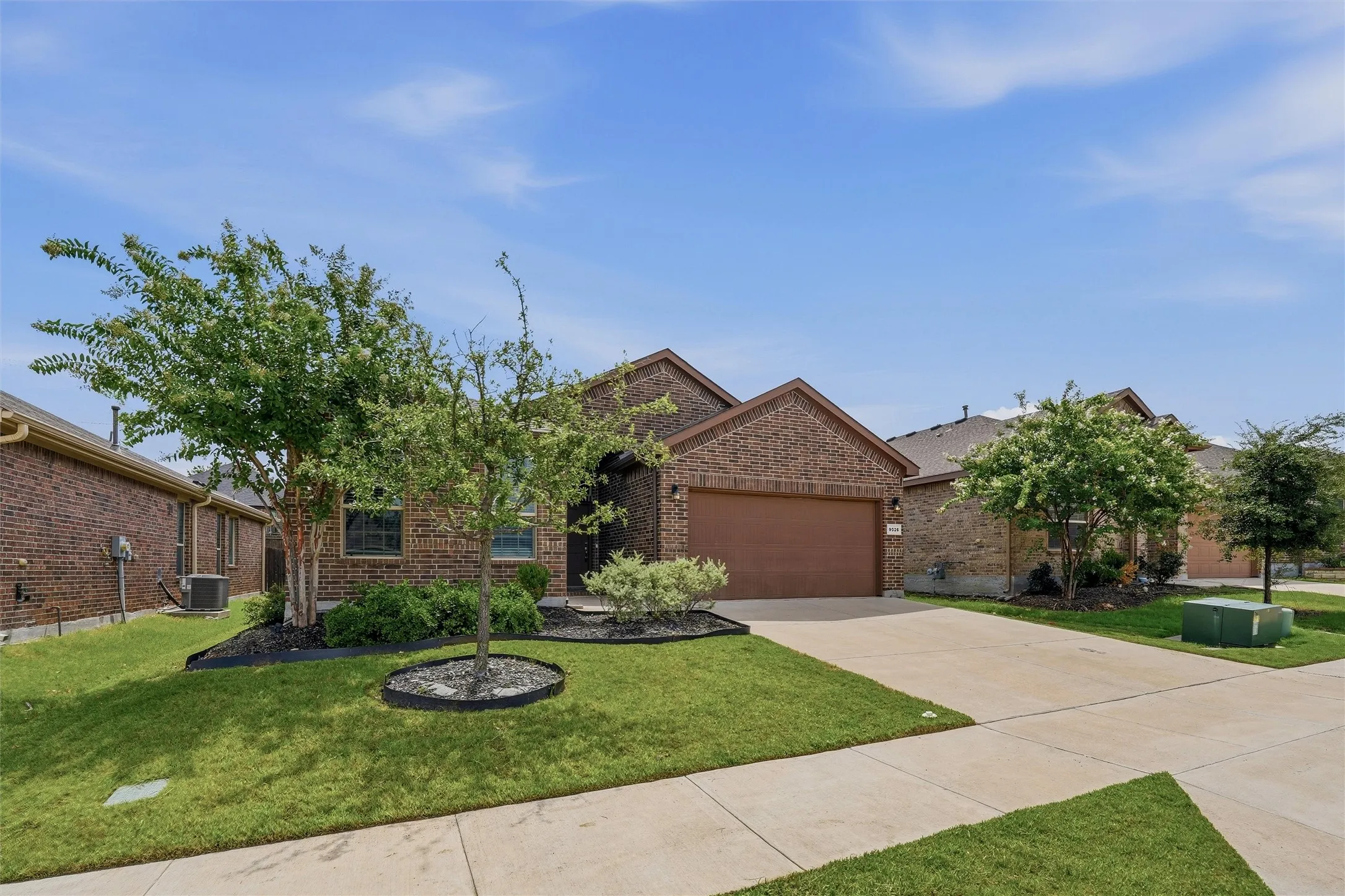Brick exterior with an attached garage, concrete driveway, and manicured landscaping